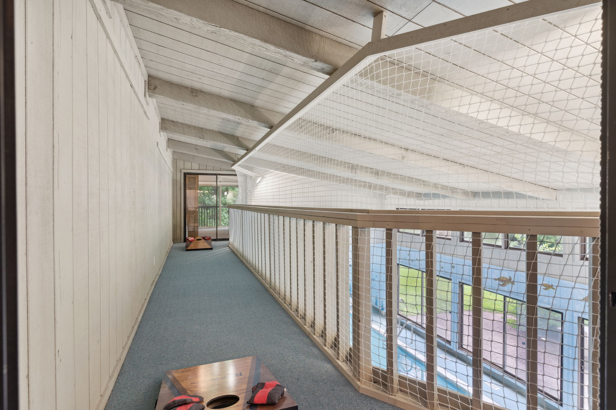 A spacious indoor balcony with a view, featuring cornhole boards and a safety net.