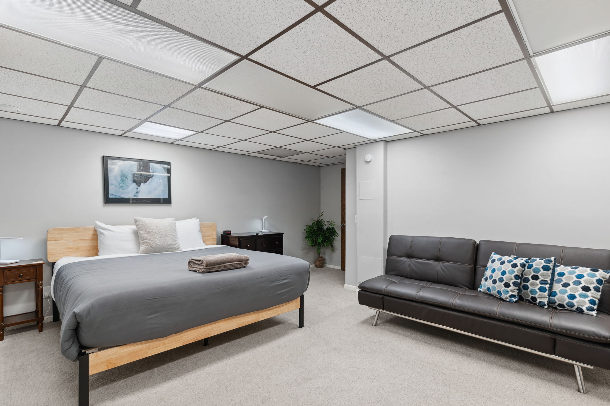 A cozy, modern basement bedroom featuring a queen bed and seating area.