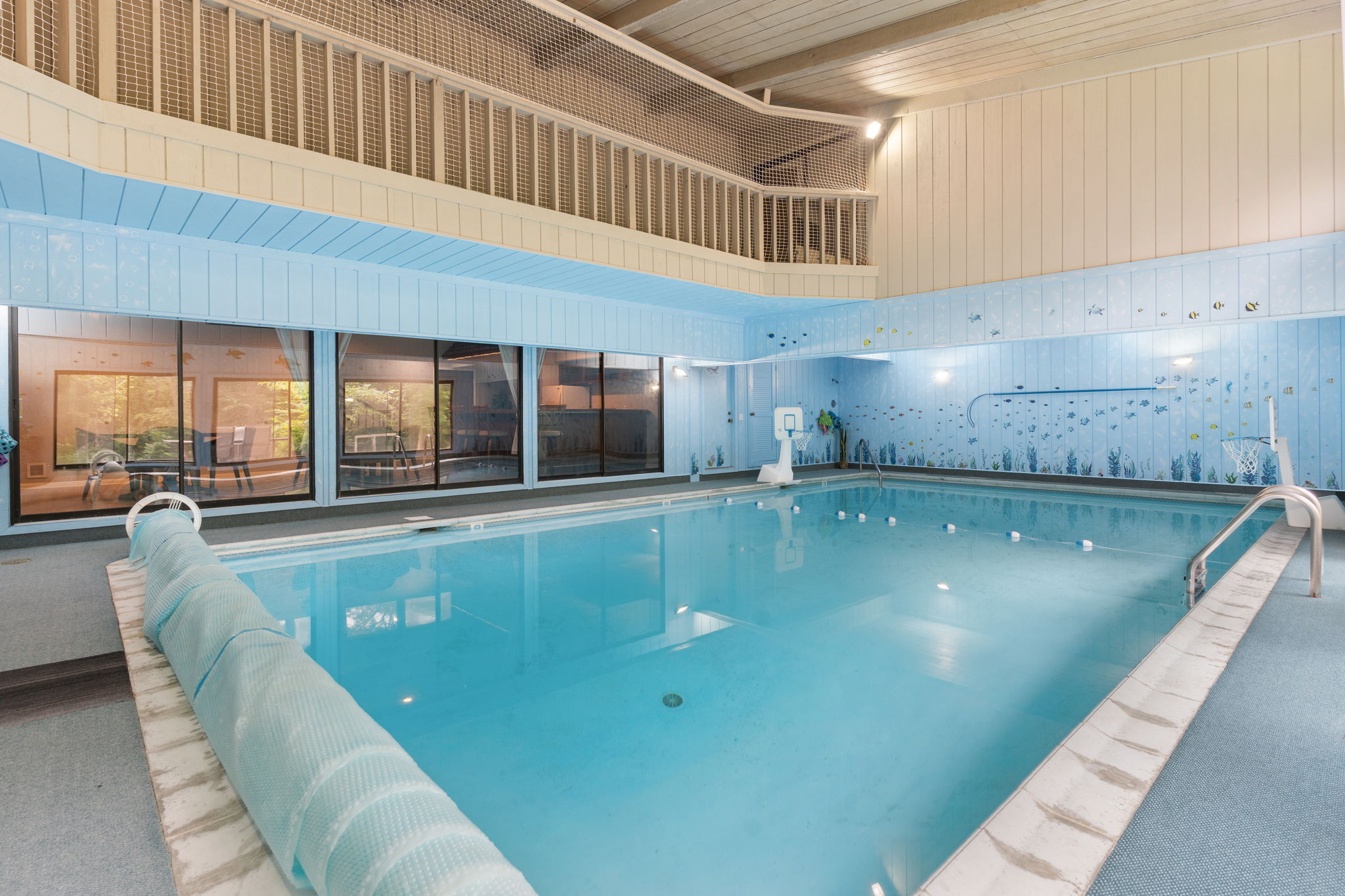 A serene indoor swimming pool adorned with aquatic murals and large windows overlooking nature.