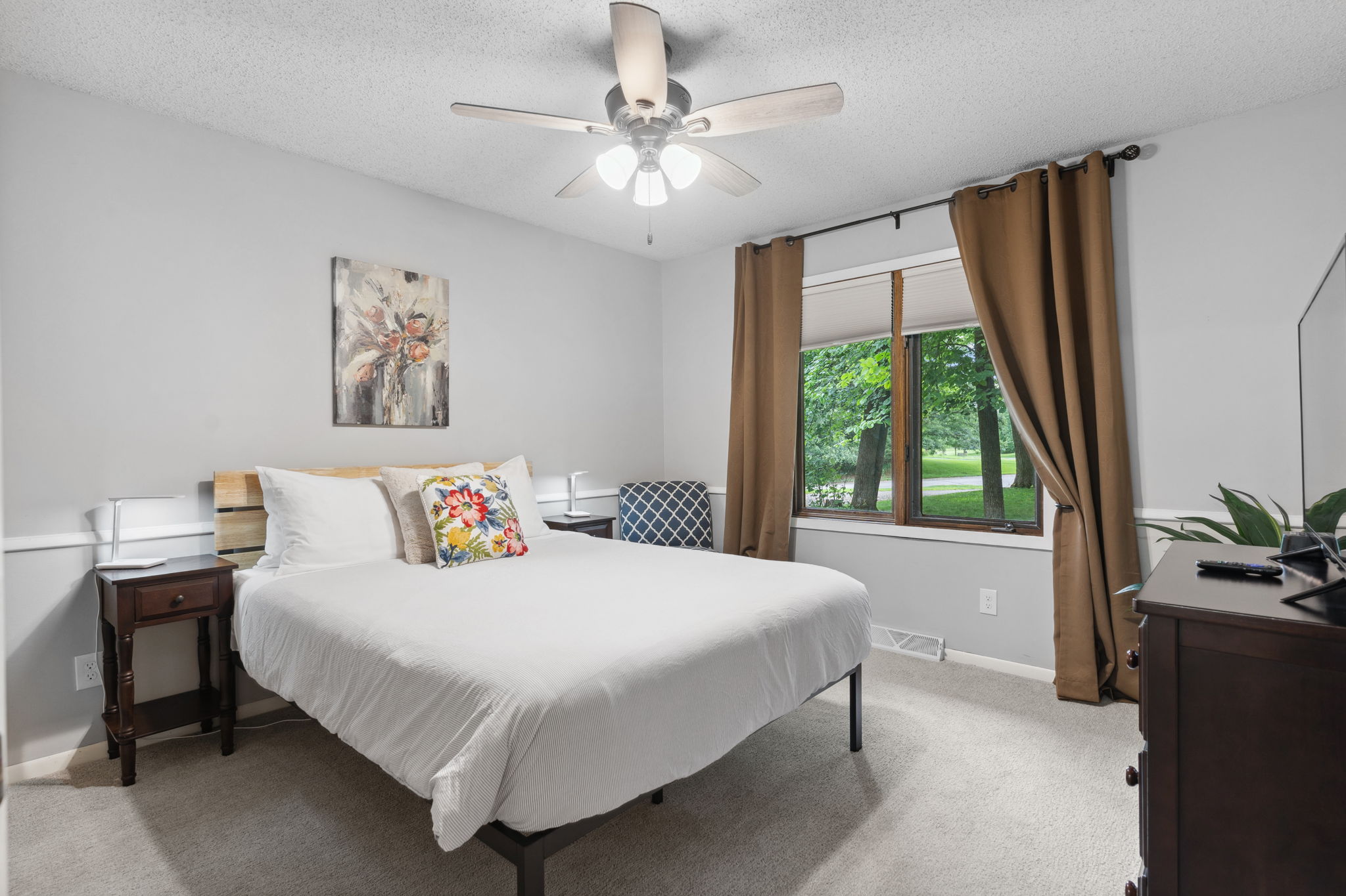 A serene and stylish bedroom featuring a cozy bed, art, and green views.