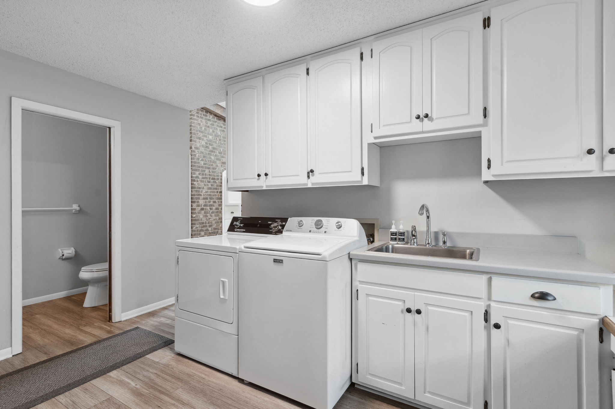 A modern laundry room with white cabinets, appliances, and a stainless steel sink.