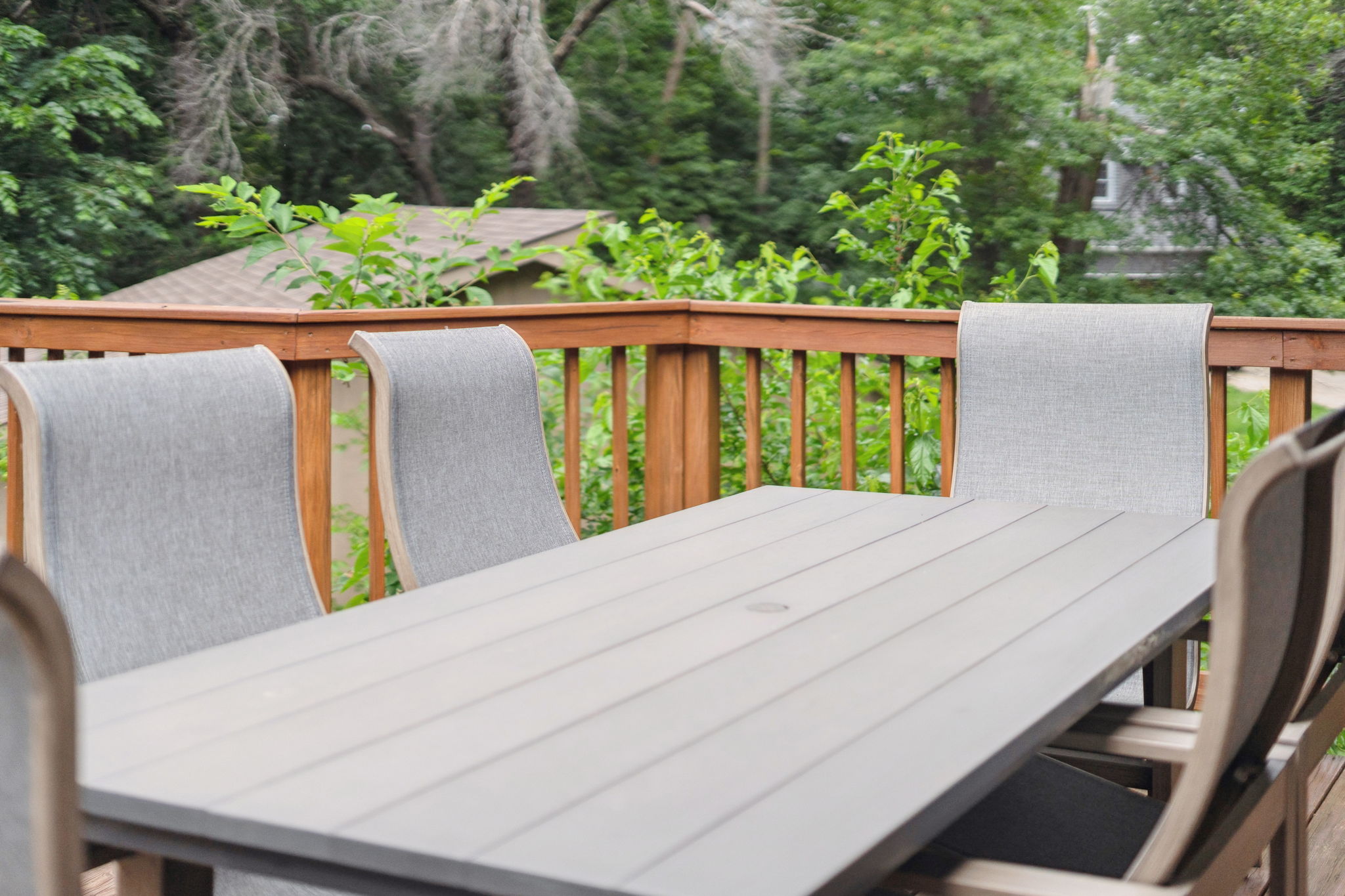 A serene outdoor dining area with a modern table and light gray chairs, surrounded by greenery.