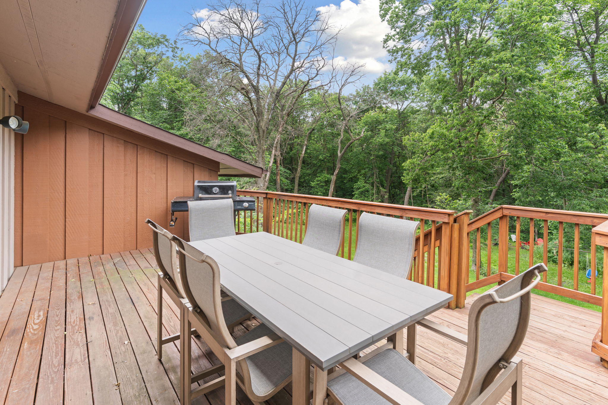 A modern outdoor dining space on a wooden deck surrounded by greenery.