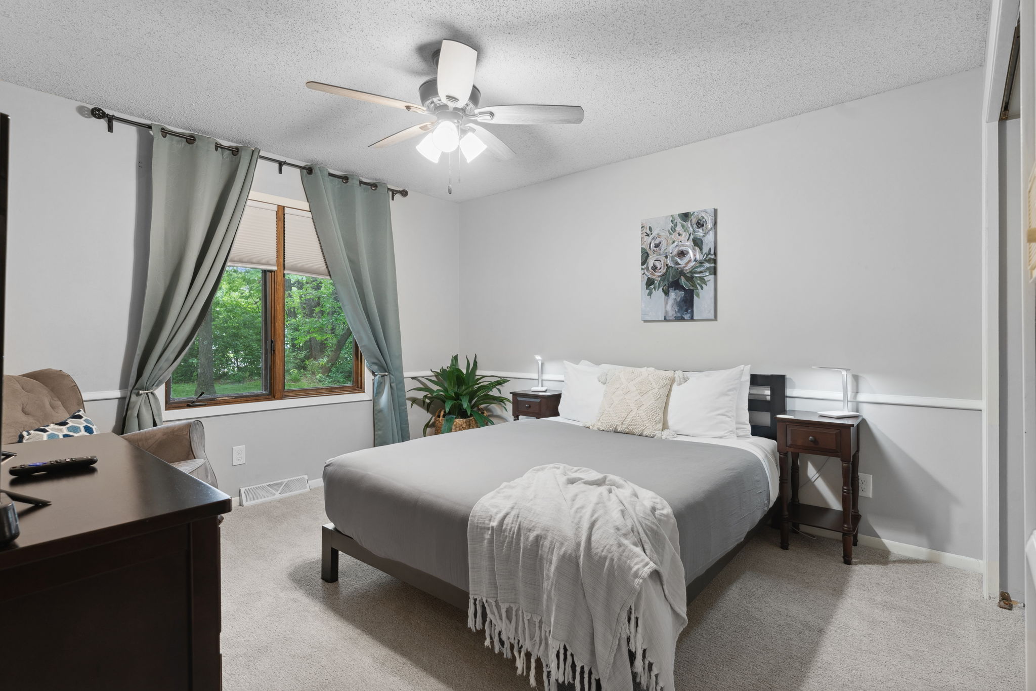 A cozy bedroom with a gray bedspread and natural light from the window.