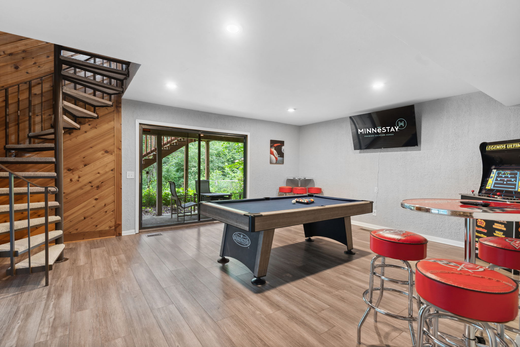 A cozy game room with a pool table and arcade machine, leading to an outdoor view.