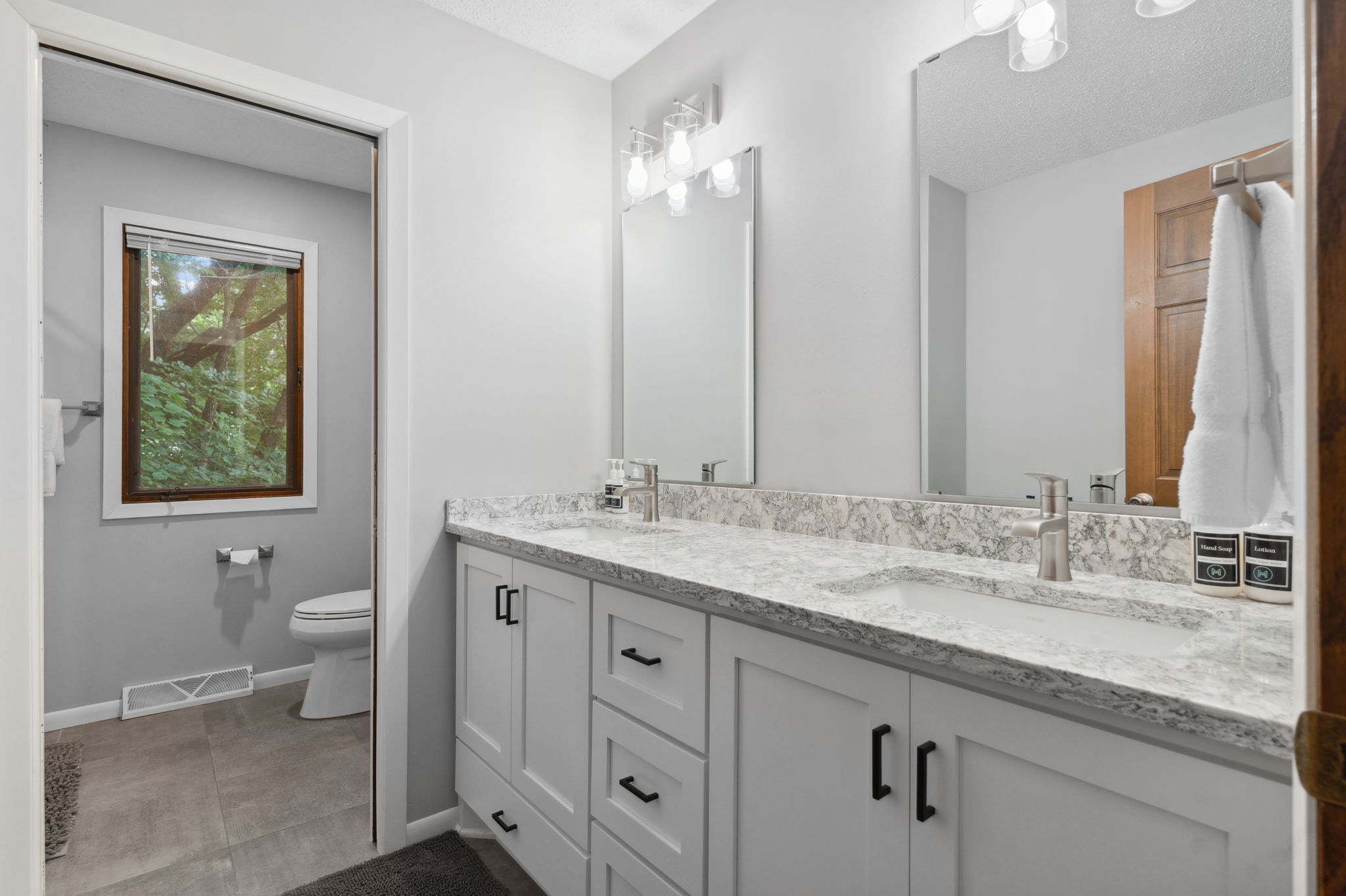 A modern bathroom featuring marble countertops and a serene view through a window.