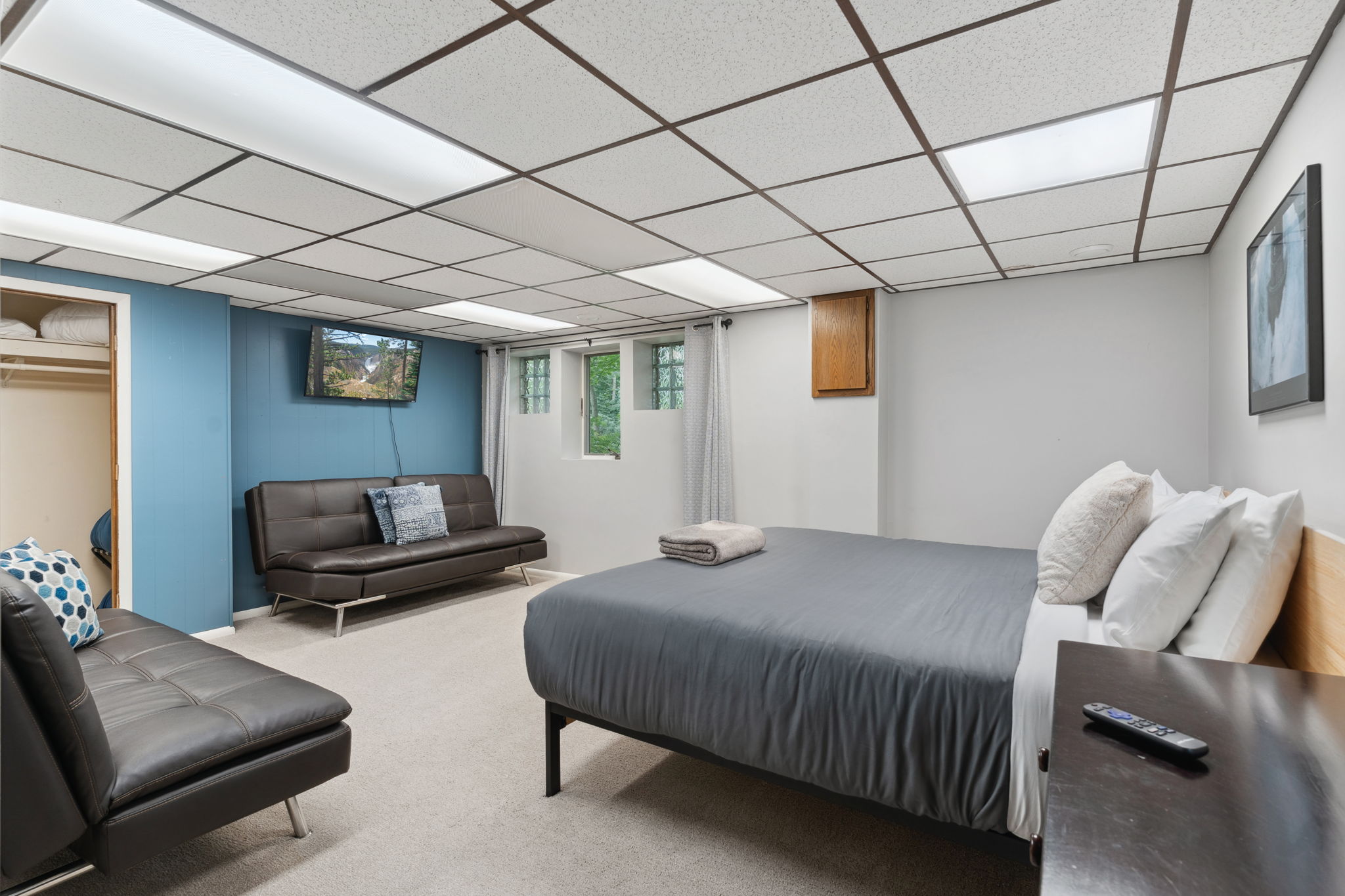 A cozy and modern basement bedroom with a bed, sofa, and TV.