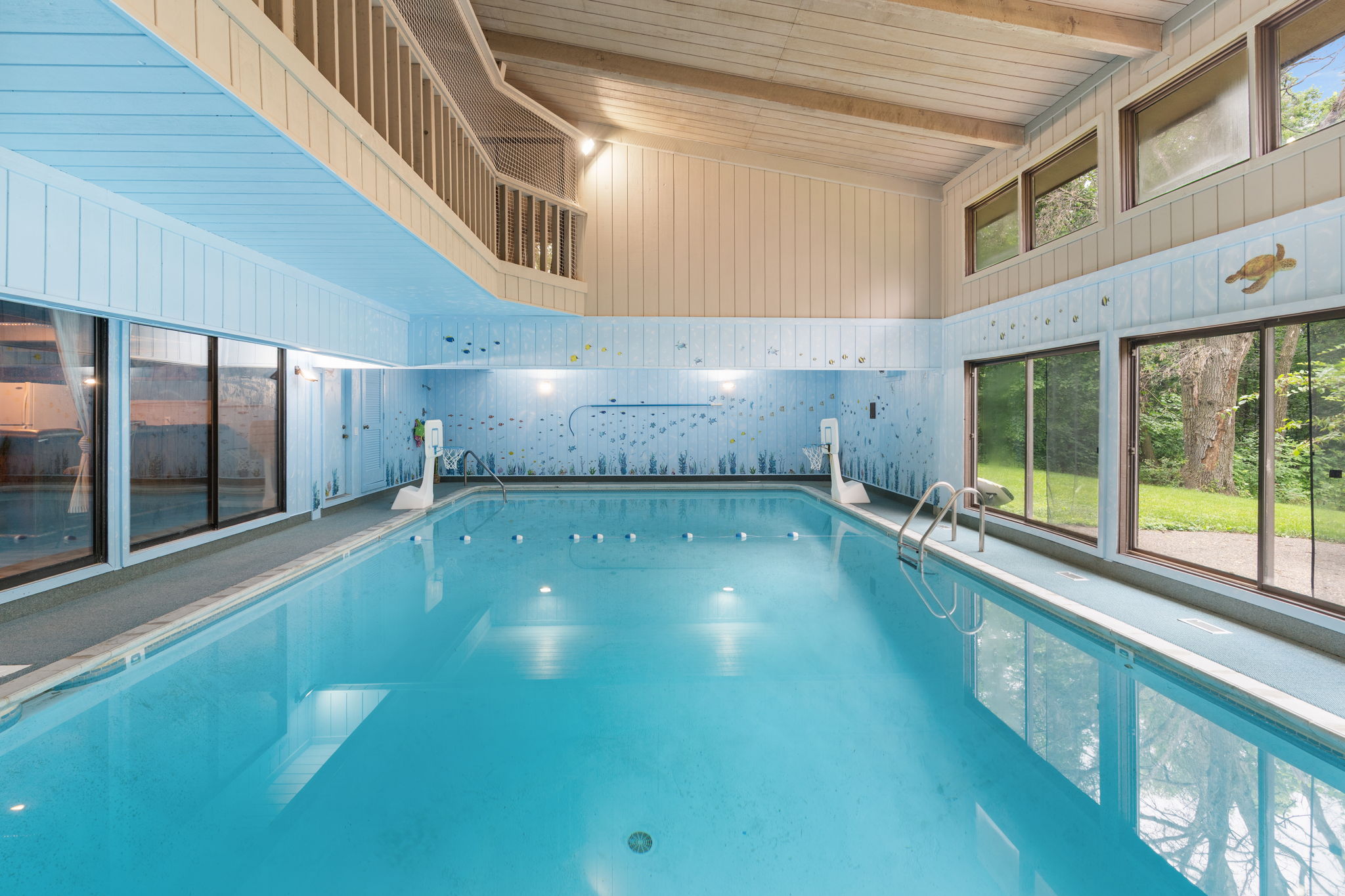 Indoor swimming pool with aquatic-themed decor and large windows overlooking a green garden.