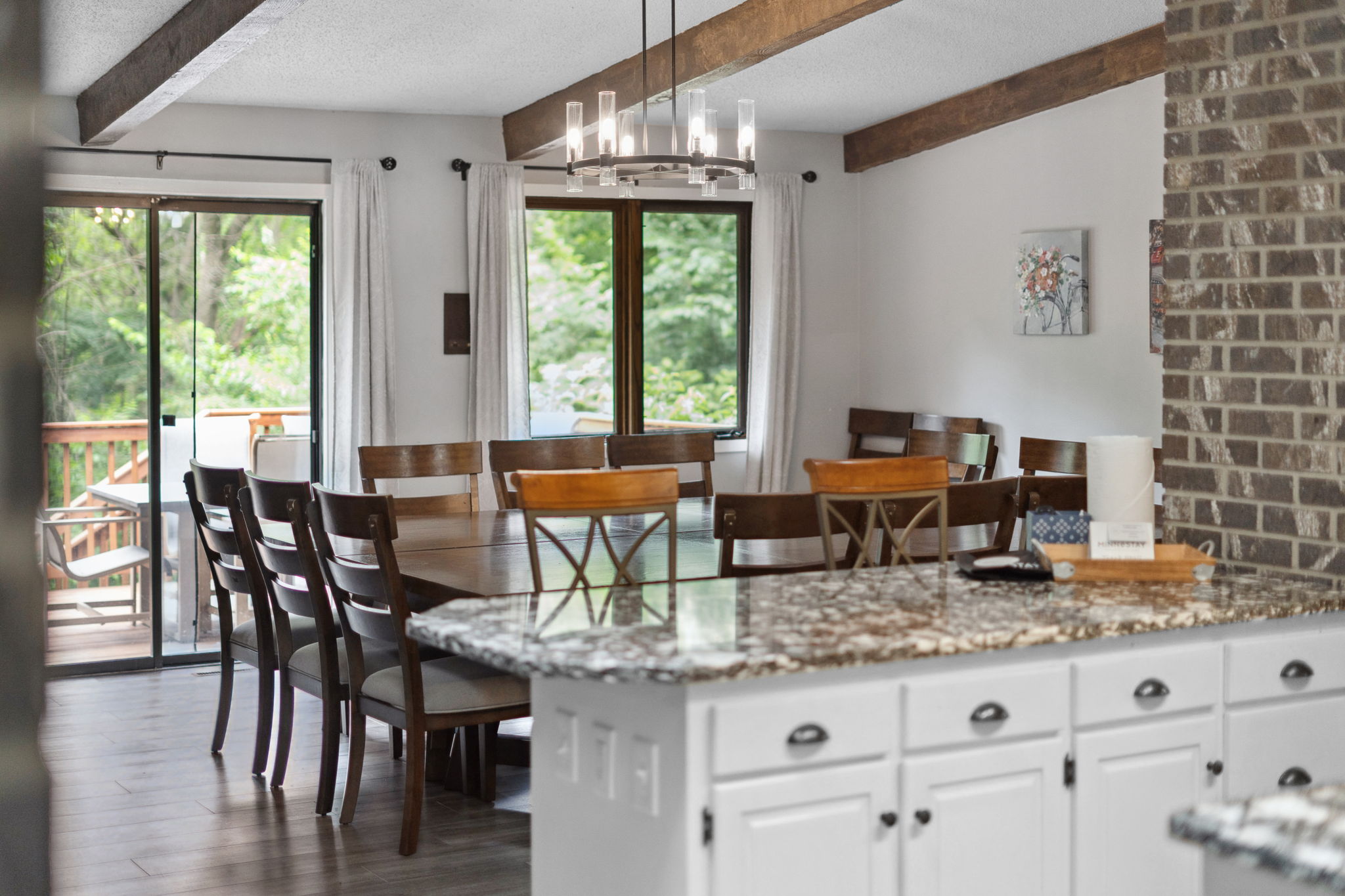 A cozy dining area with a large wooden table and modern chandelier, filled with natural light.