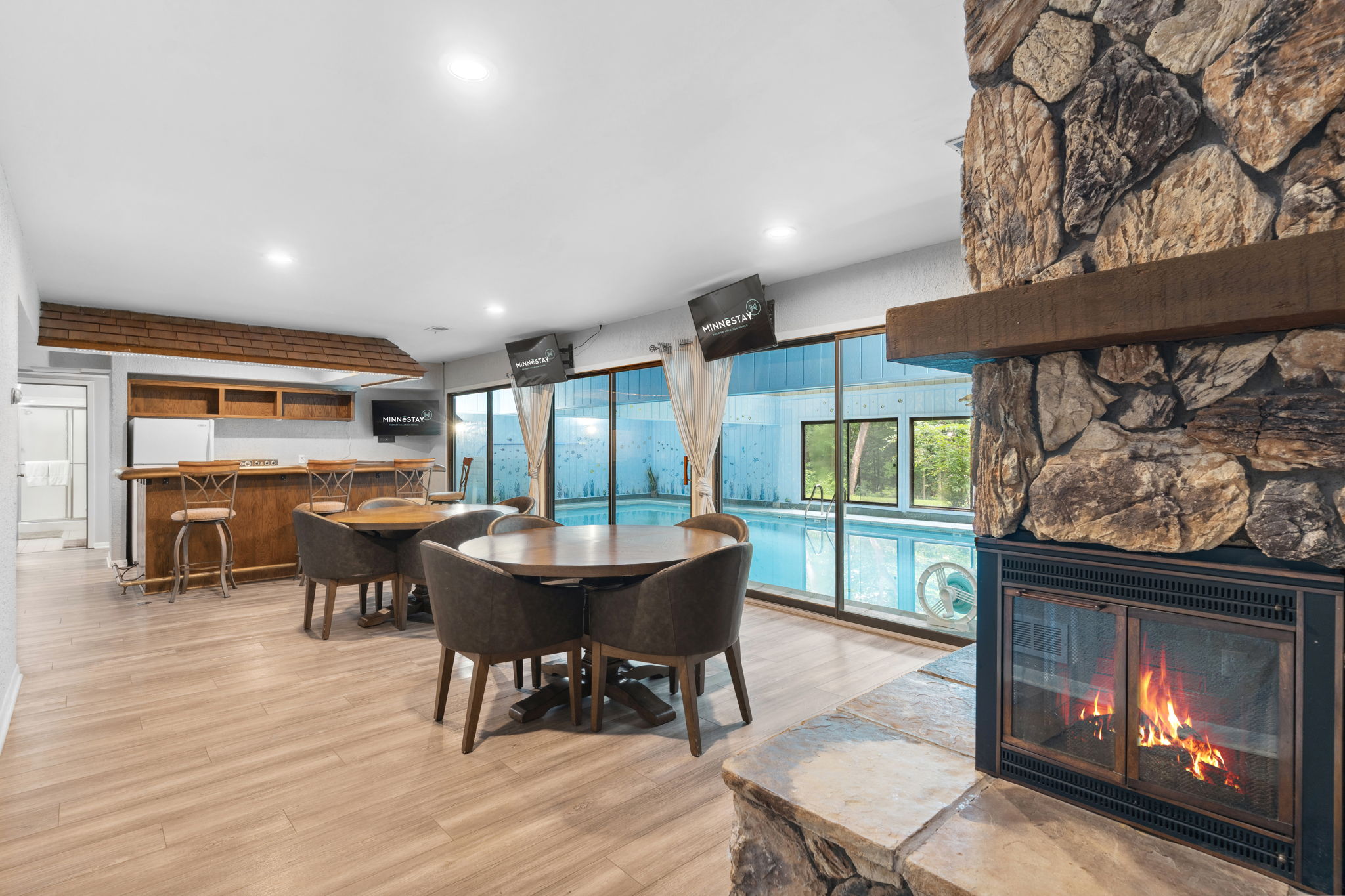 A modern indoor space featuring a cozy bar, dining area, and a shimmering swimming pool.