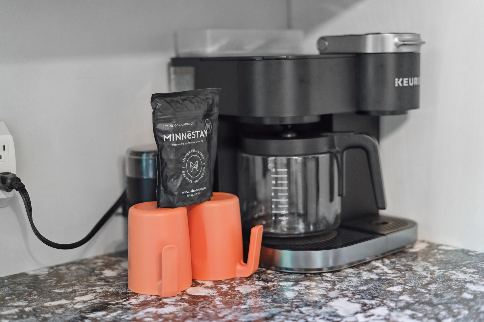 A modern coffee setup with a Keurig machine, orange cups, and Minnestay coffee.