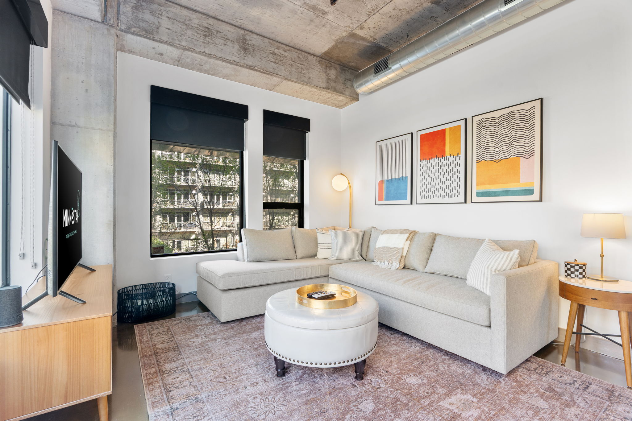 Modern living room with a grey sectional sofa, abstract art, and large windows.