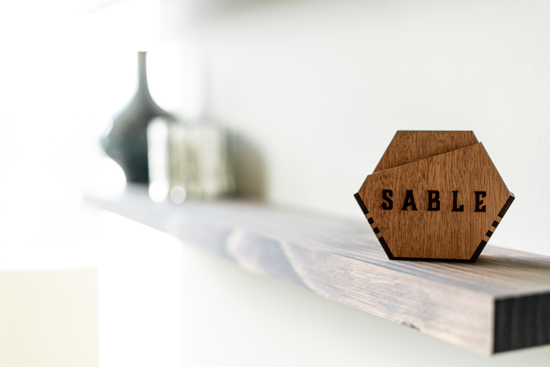 A decorative wooden piece shaped like a hexagon with 'SABLE' etched on it, displayed on a modern shelf.