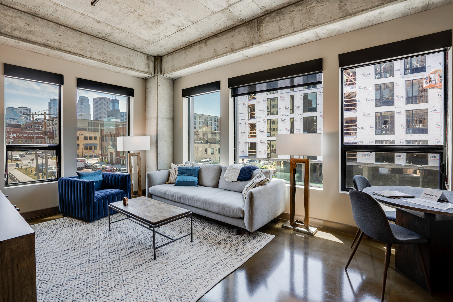 A stylish and modern apartment living area with exposed concrete elements and a view of the city skyline.