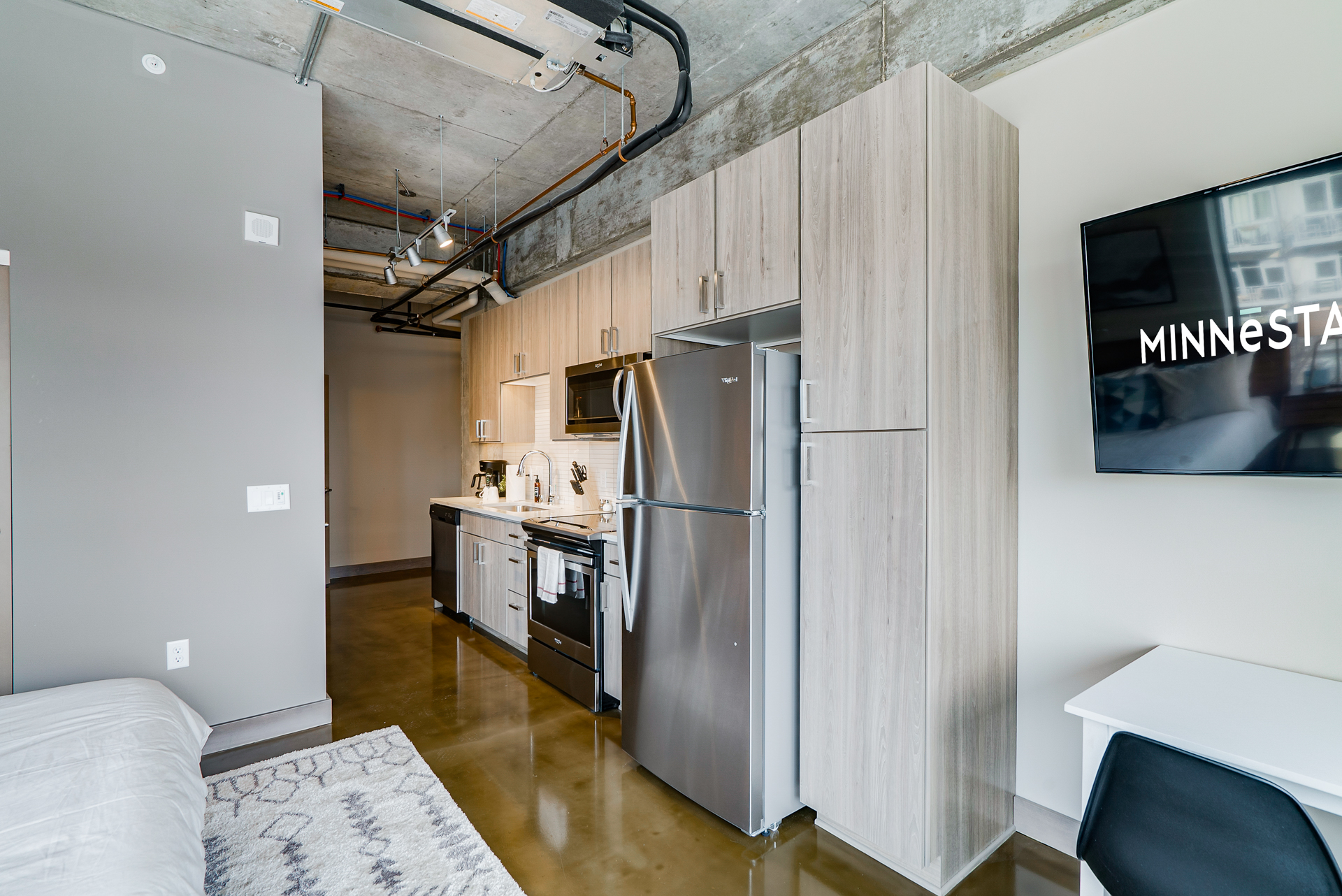 A modern studio apartment with an industrial aesthetic, featuring a sleek kitchen and workspace.