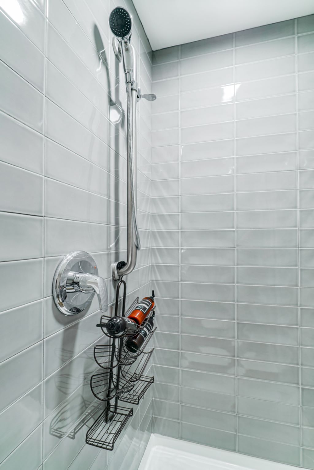 A modern shower with chrome fixtures and gray tiles, featuring an organized product rack.