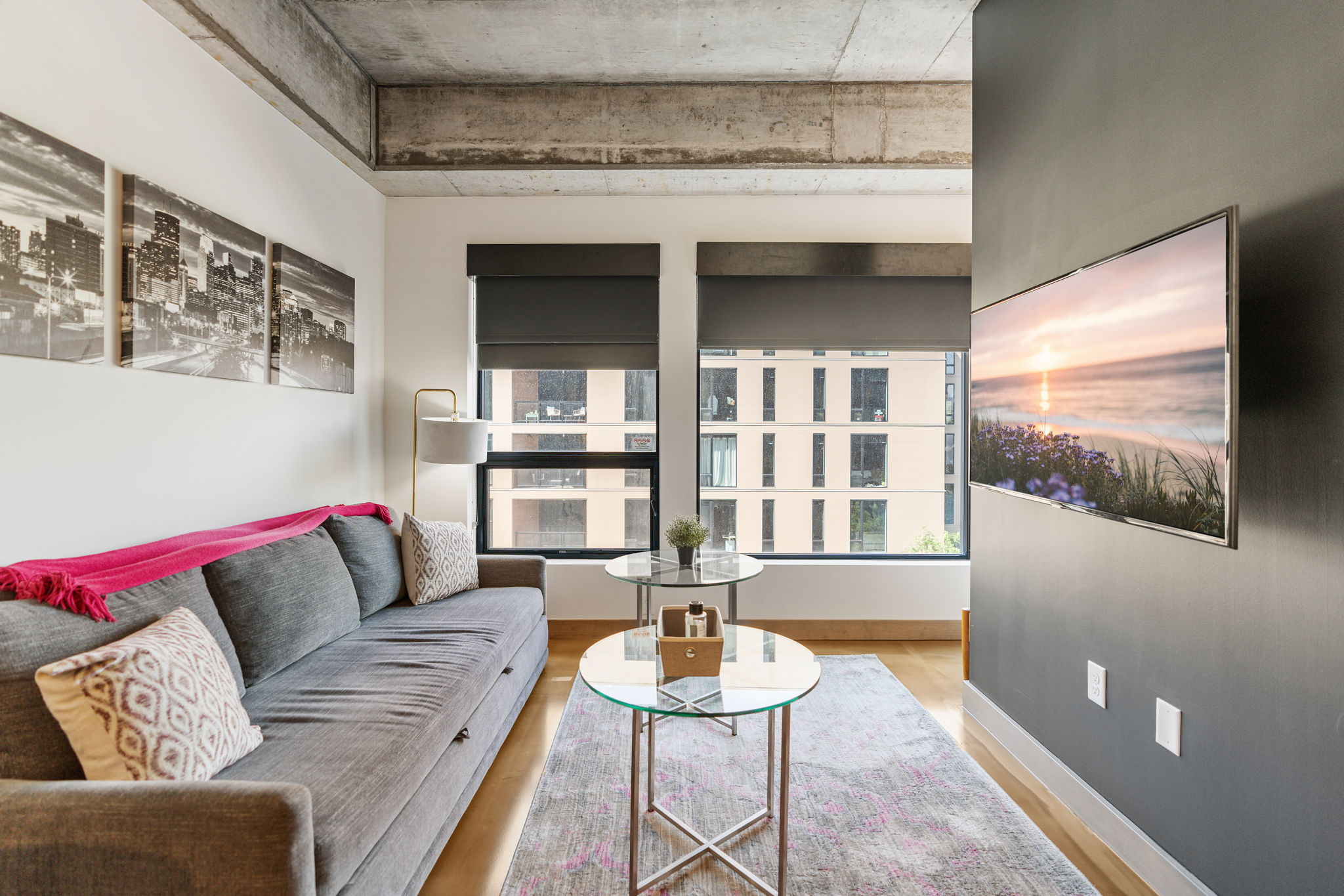 A modern living room featuring a gray couch, glass coffee tables, and cityscape art.