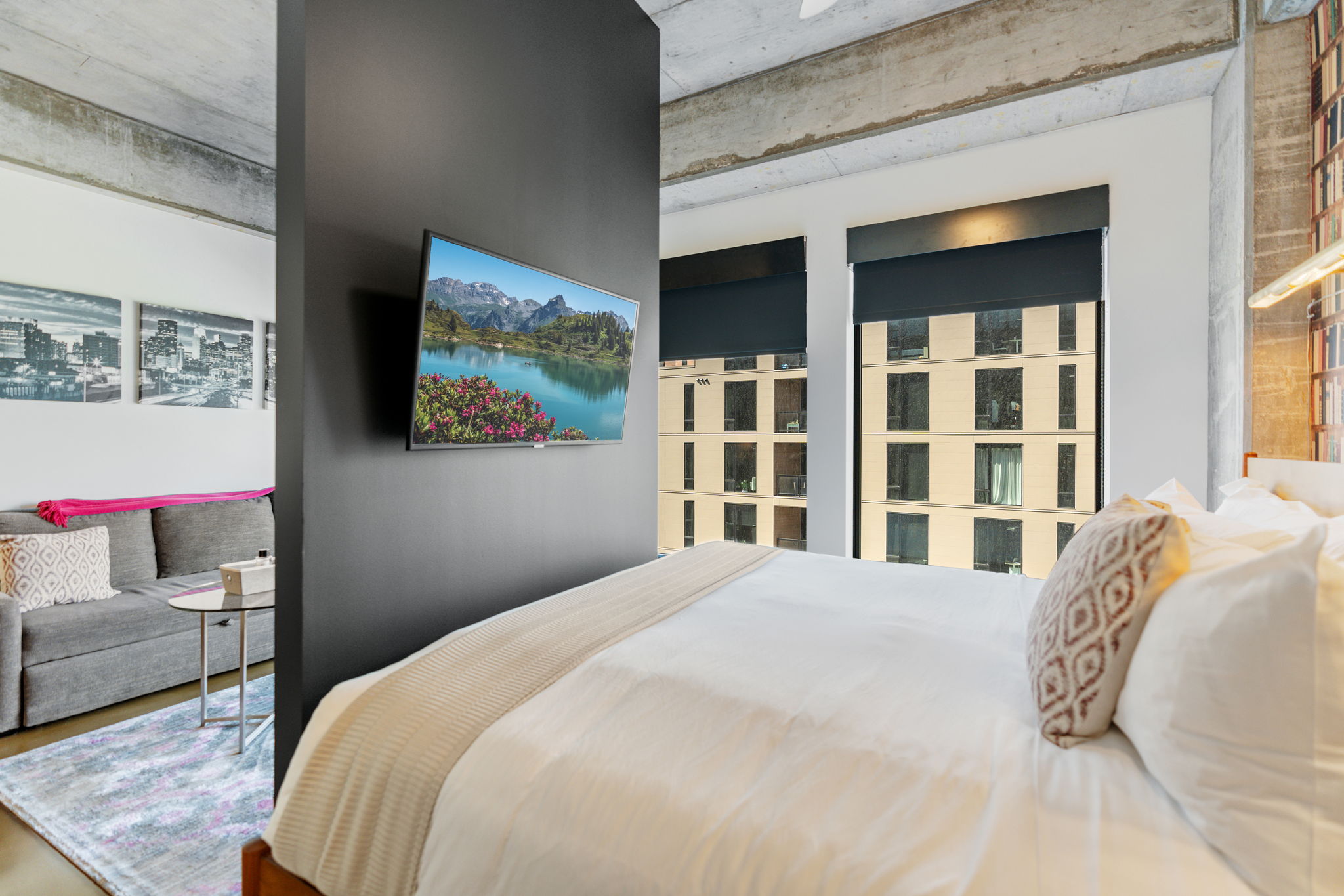 A modern studio apartment with a cozy bedroom and living area, featuring a flat-screen TV and city views.