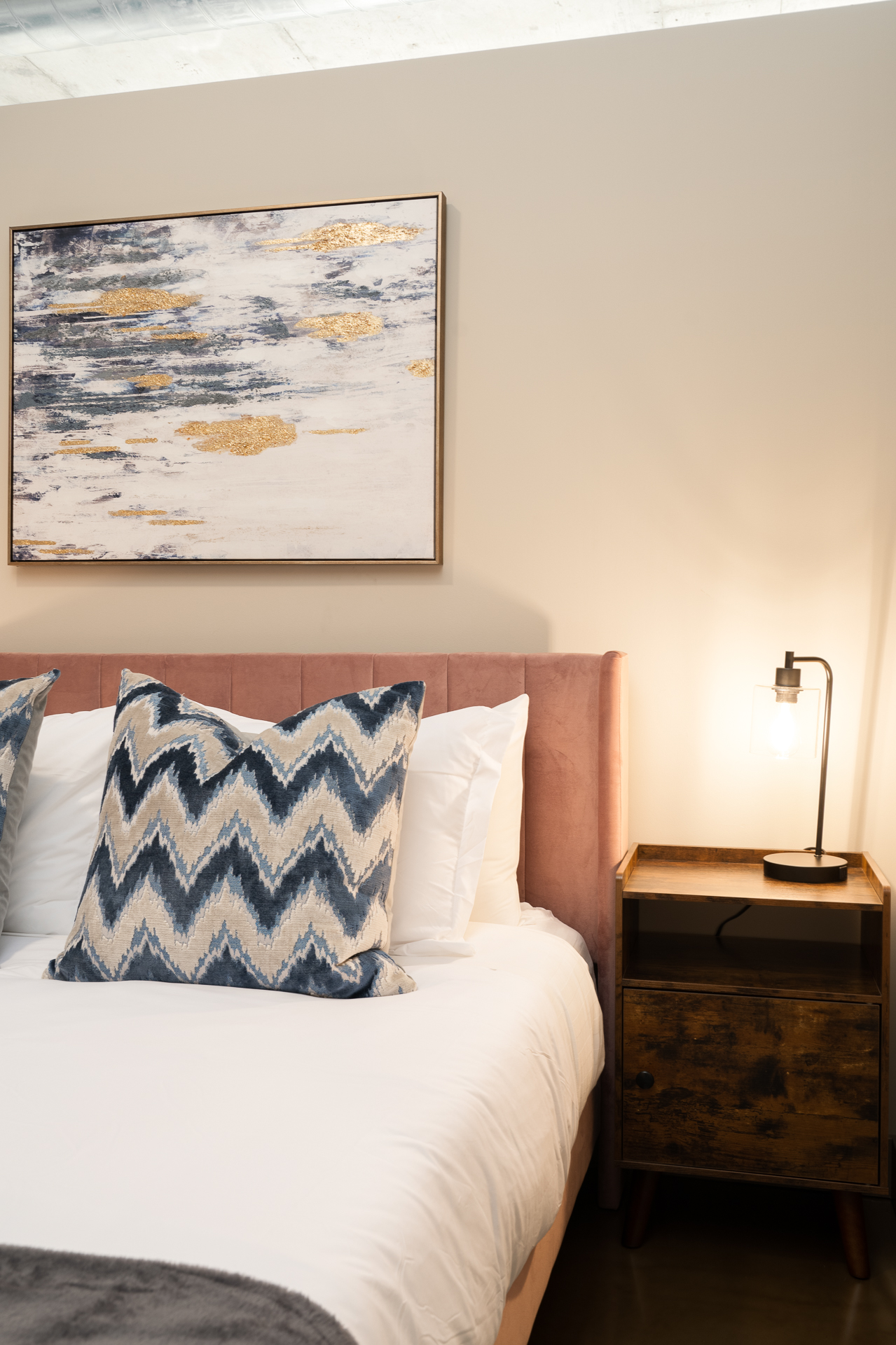 A stylish and inviting bedroom featuring a pink upholstered headboard and decorative zigzag pillows.
