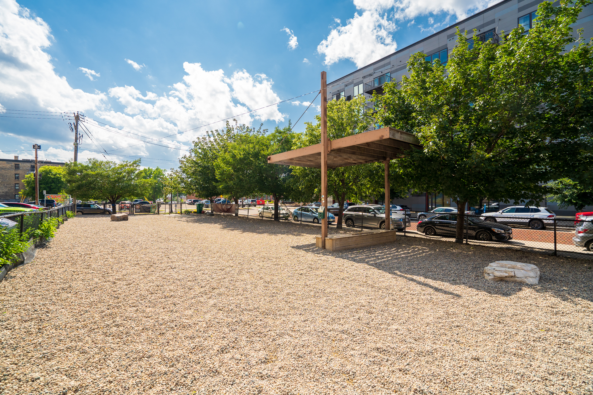 A sunny park area featuring gravel ground and a wooden structure for shade.