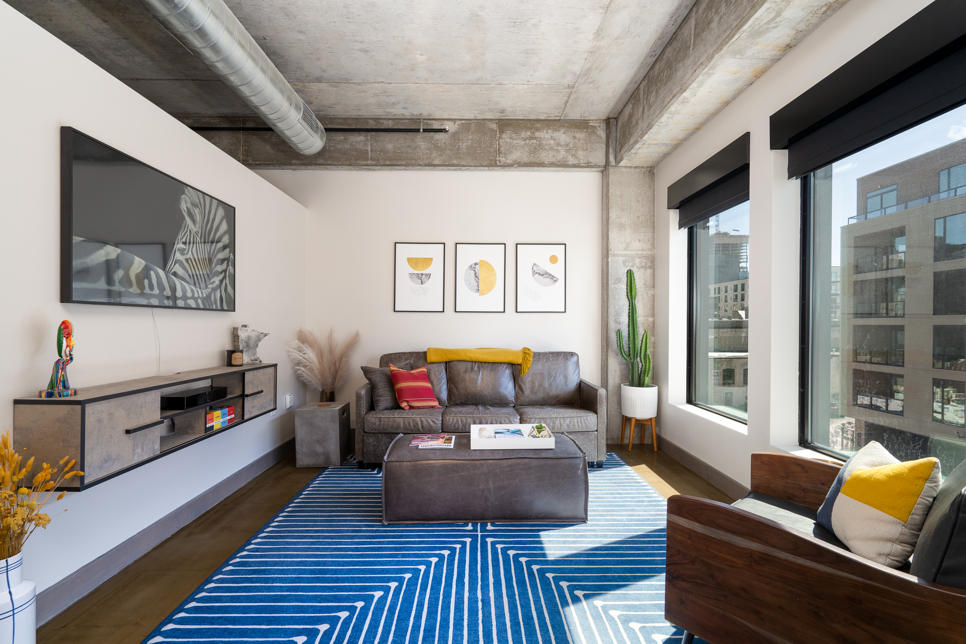 A sleek, modern living room featuring a leather couch, geometric rug, and city view.