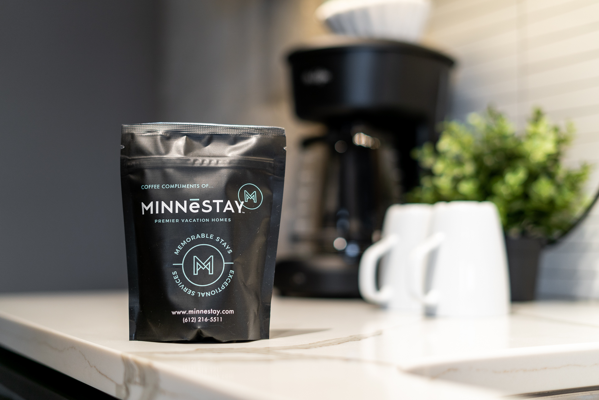 Coffee bag from Minnestay on a modern countertop with coffee mugs and a plant.