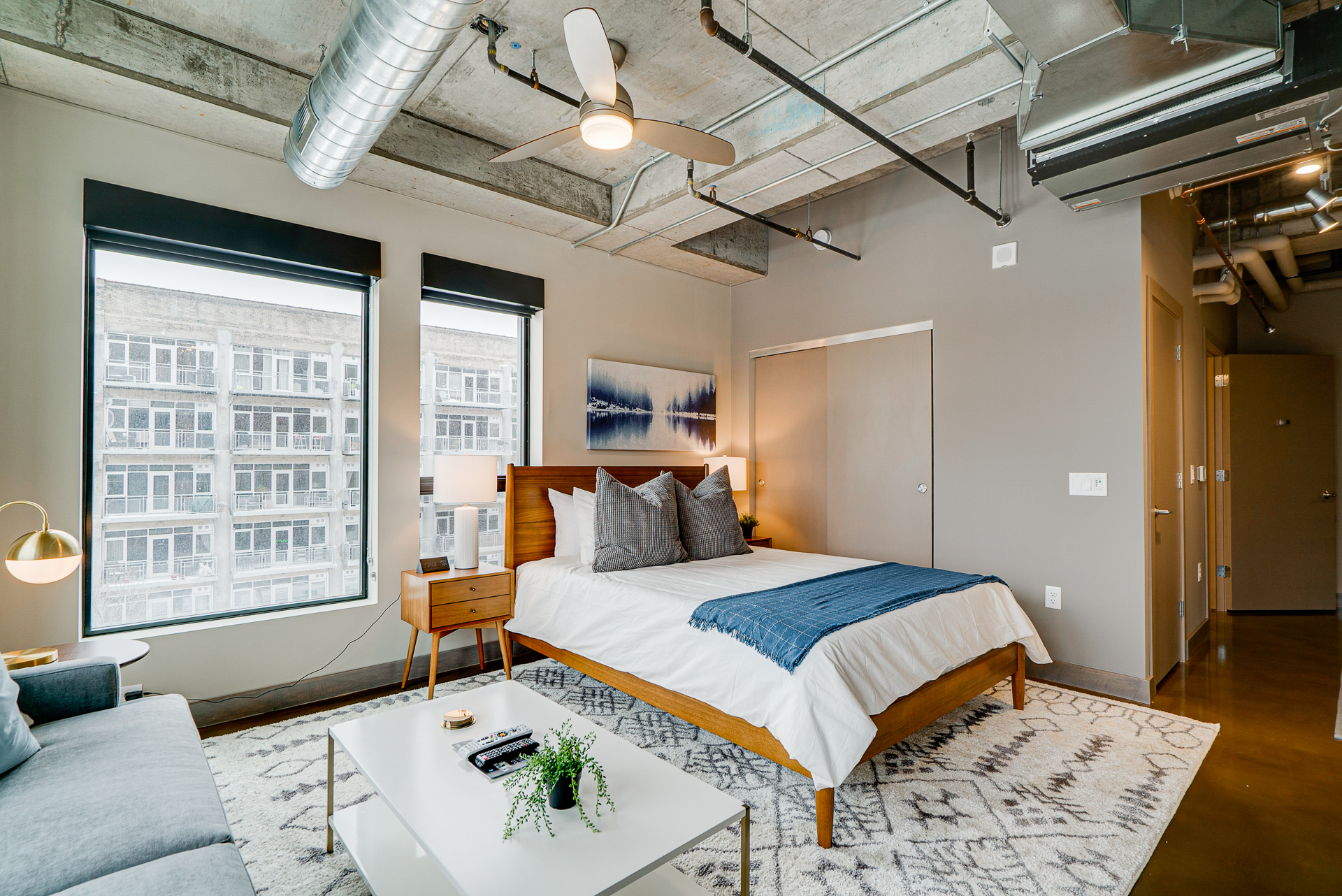 A modern bedroom featuring a cozy bed and inviting seating area with large windows.