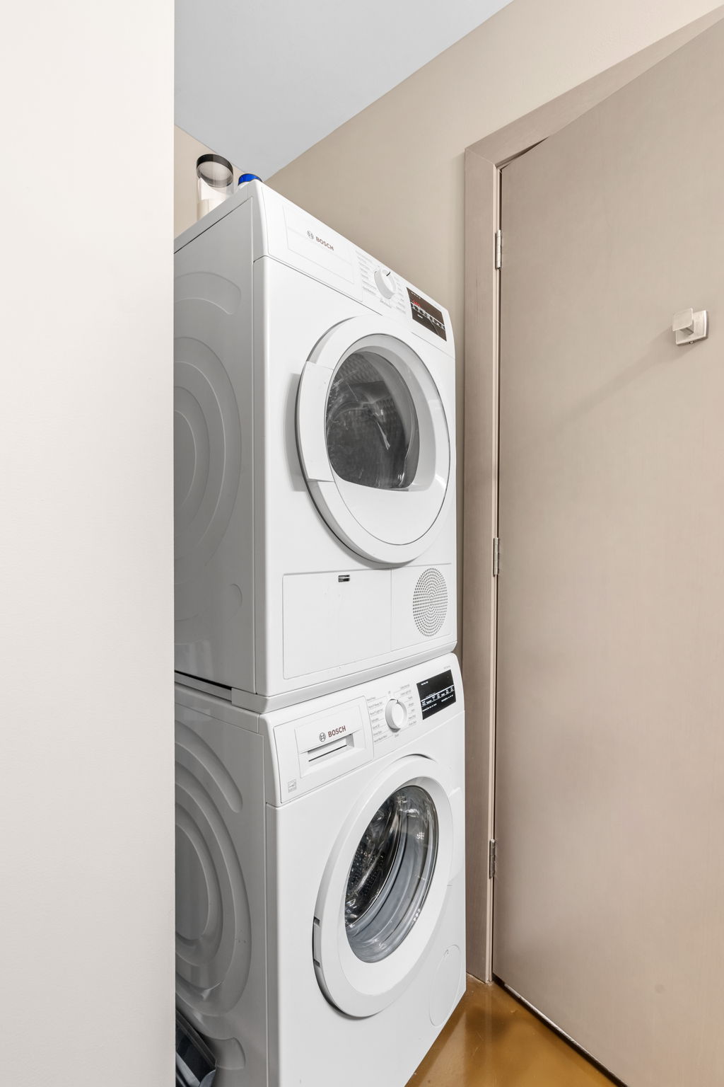 Compact and modern stacked washing machines in a laundry nook.