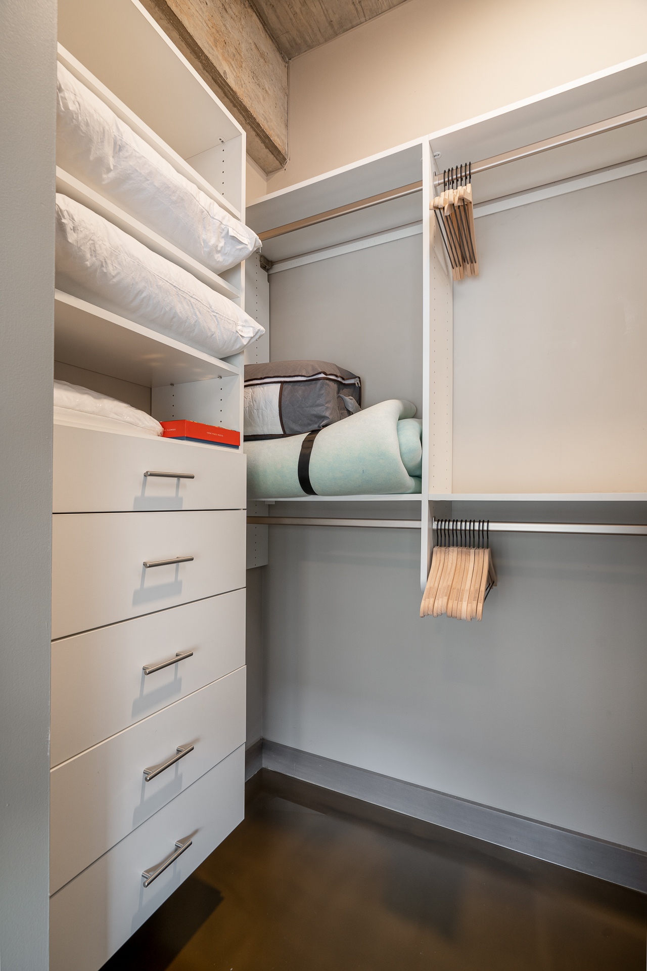 A modern, organized closet showcasing white pillows, storage drawers, and wooden hangers.