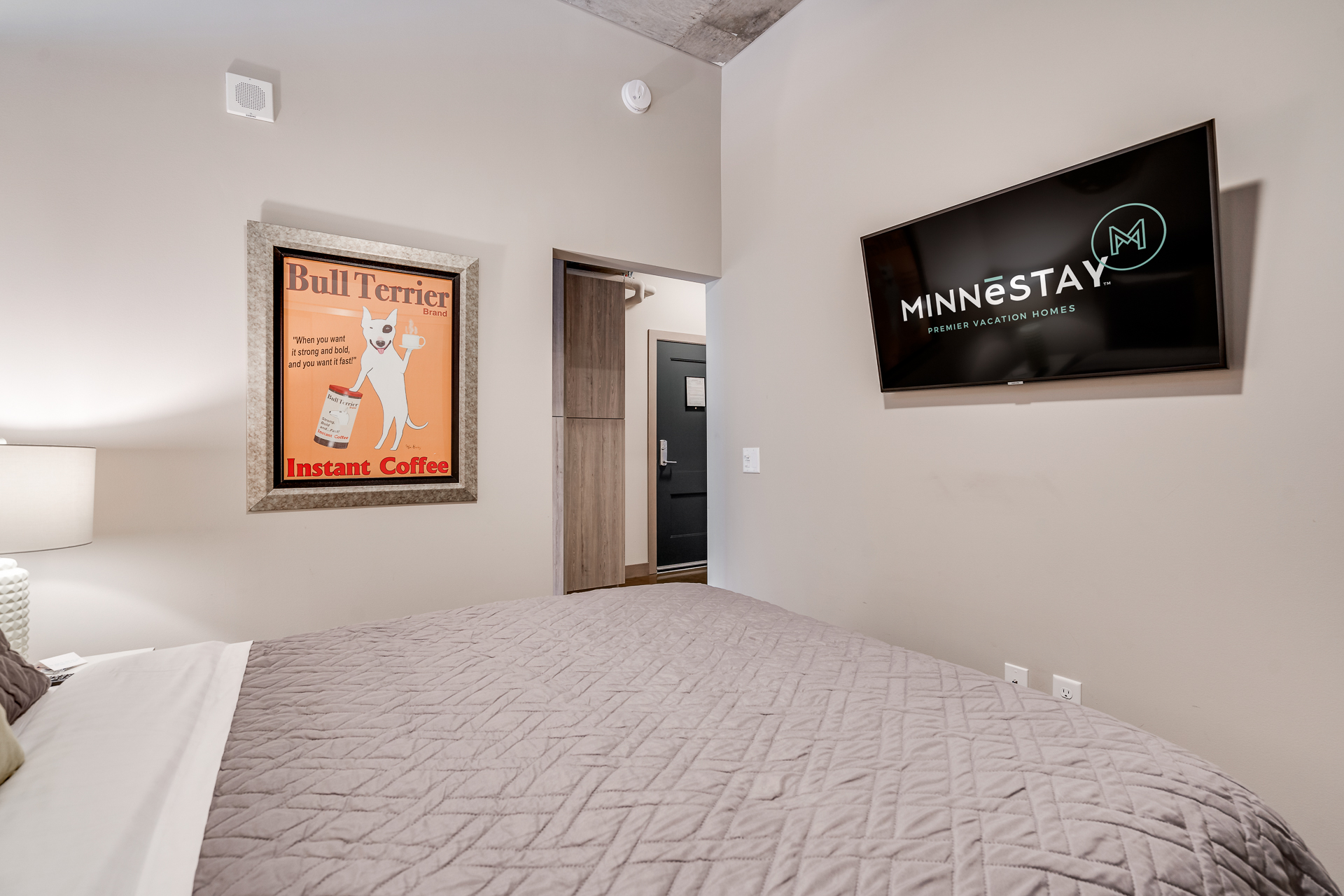 A modern bedroom featuring a vintage coffee poster and a TV with MINNESTAY branding.