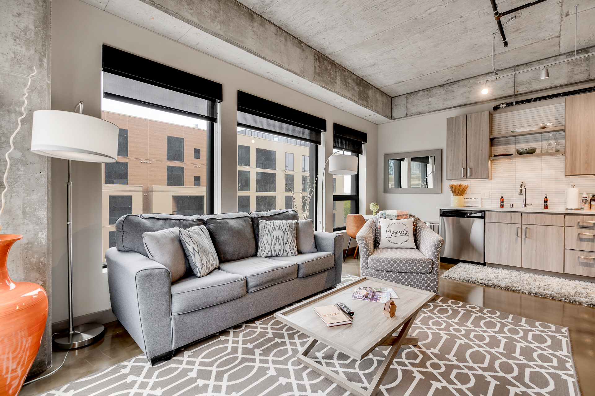 A contemporary apartment living room featuring a gray sofa, accent chair, and kitchenette.