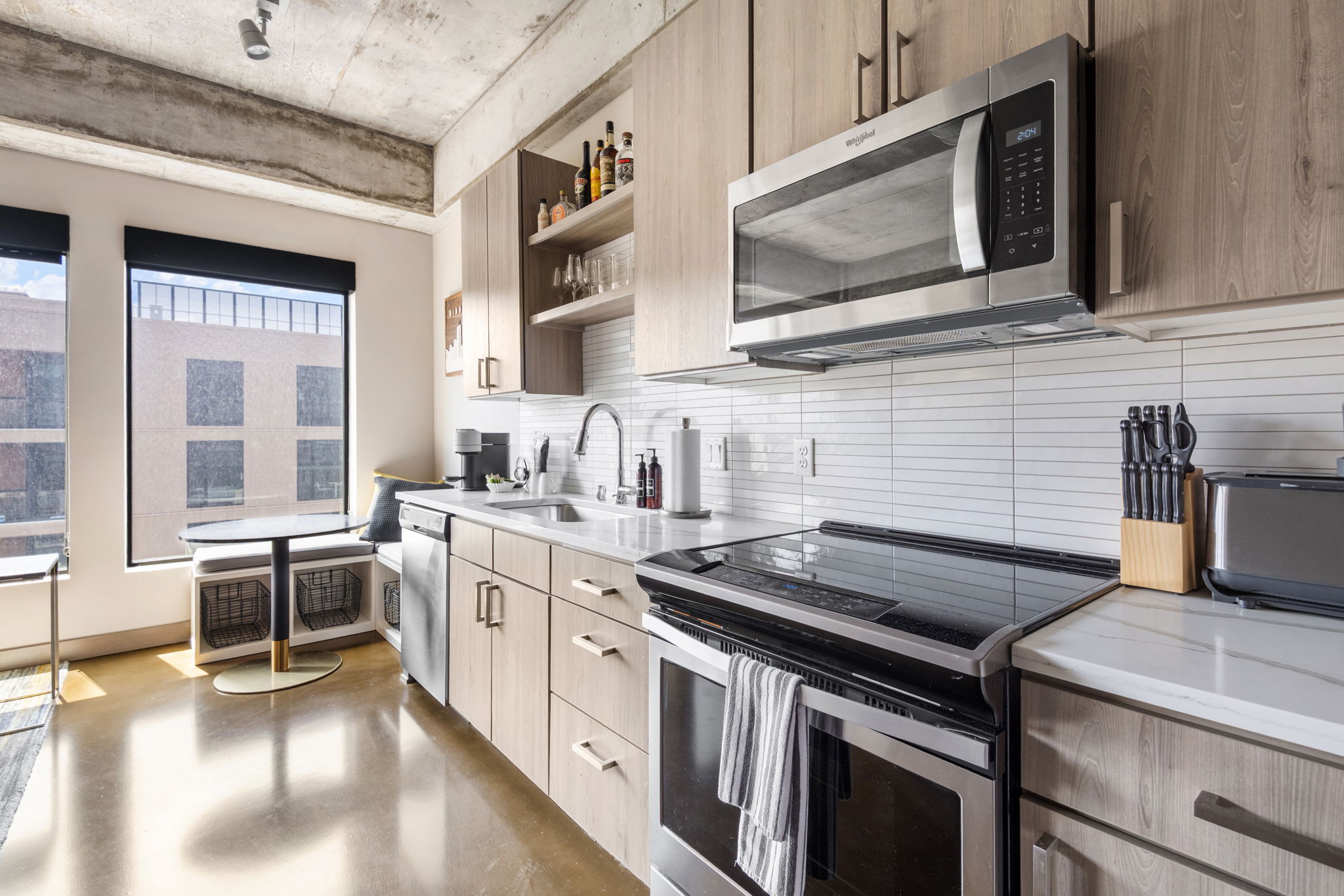 A modern kitchen with light wood cabinetry and stainless steel appliances, bathed in natural light.