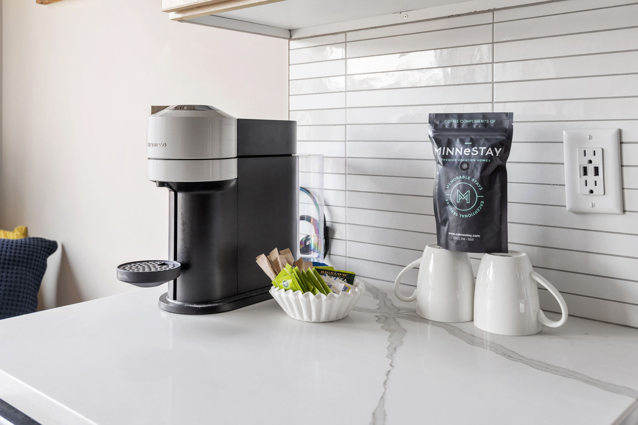 A modern coffee station featuring a Nespresso machine, tea and sugar, and elegant mugs.