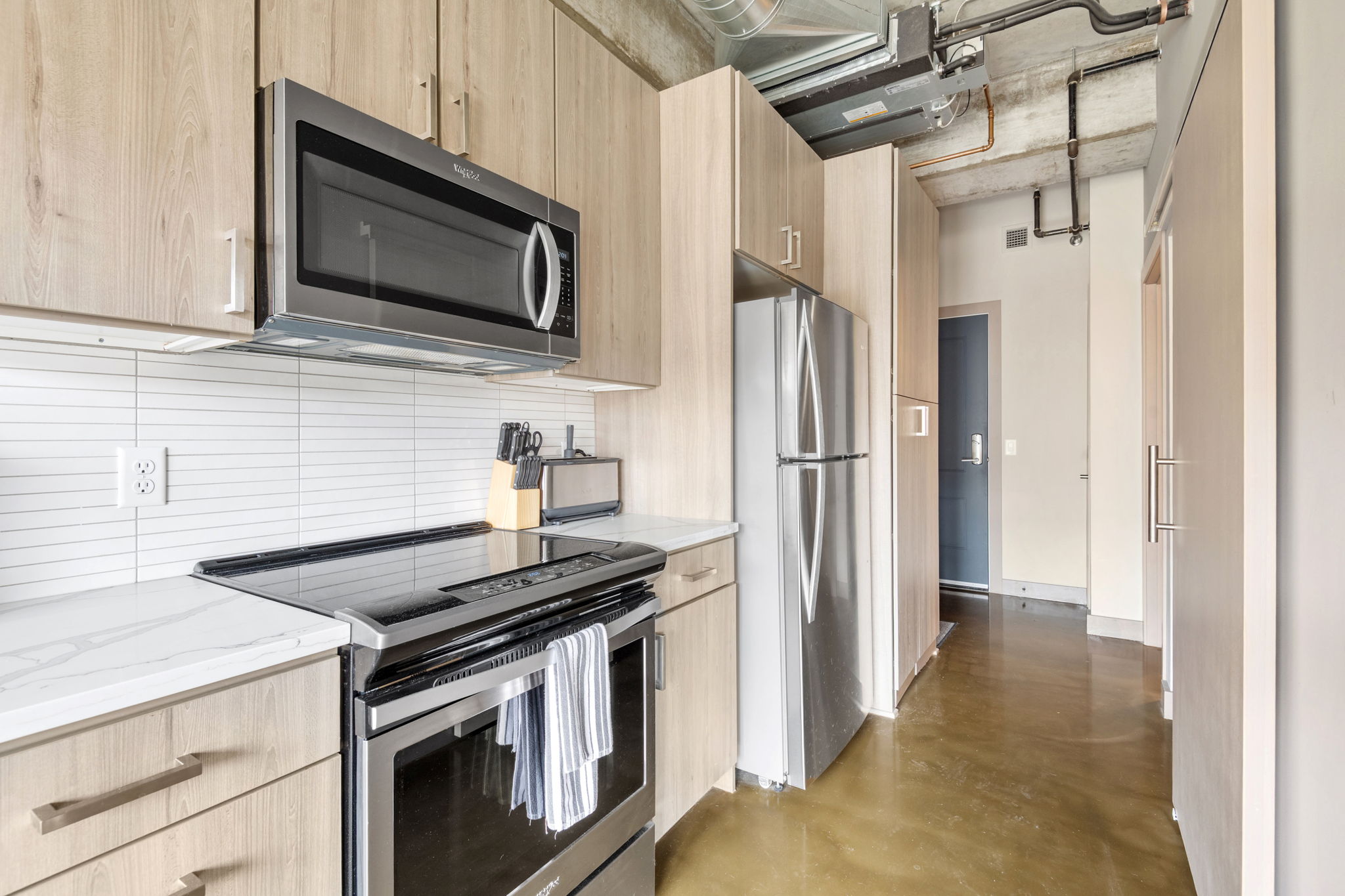 A modern kitchen with light wood cabinetry and stainless steel appliances.