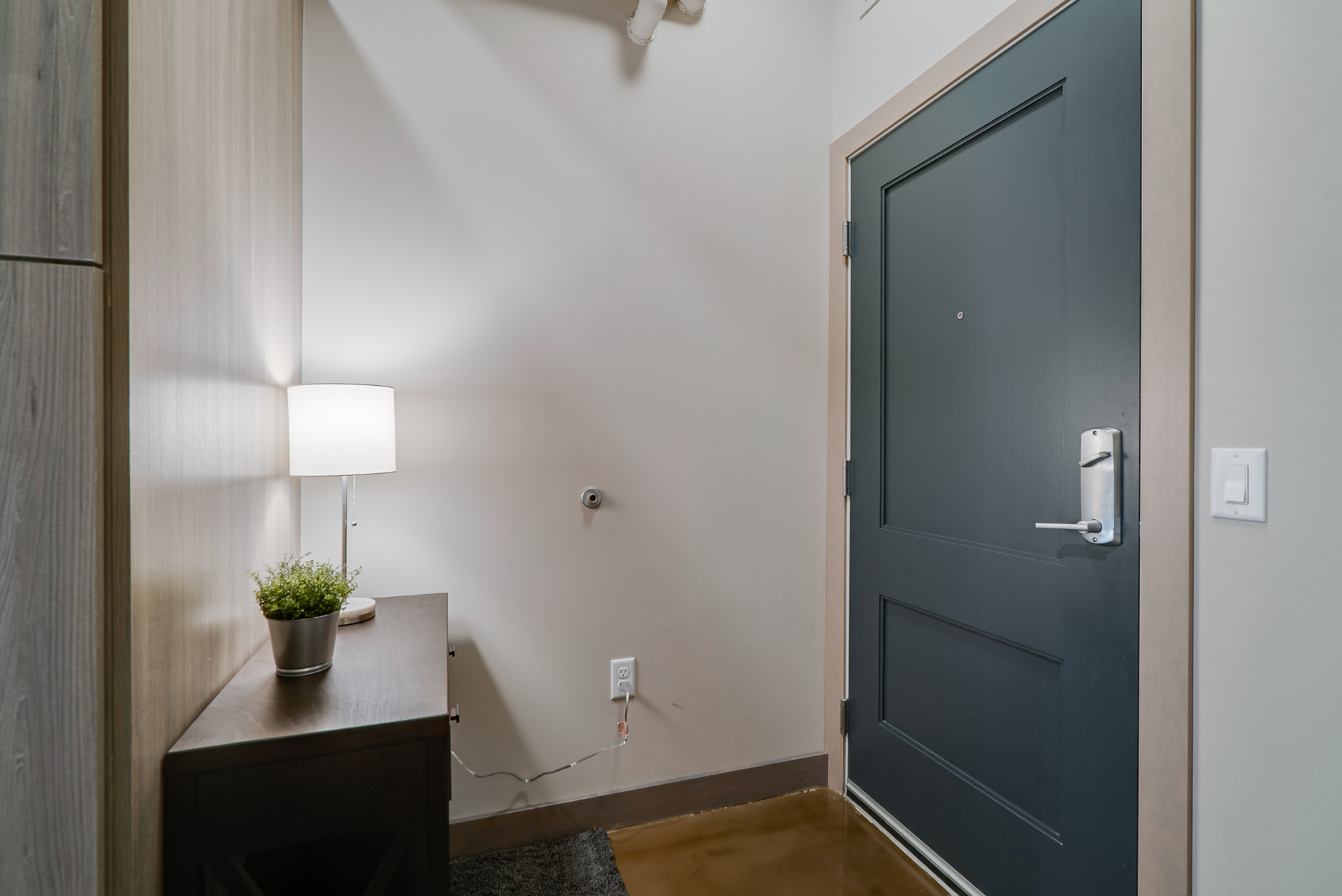 A modern apartment entryway featuring a console table, lamp, and a navy blue door.