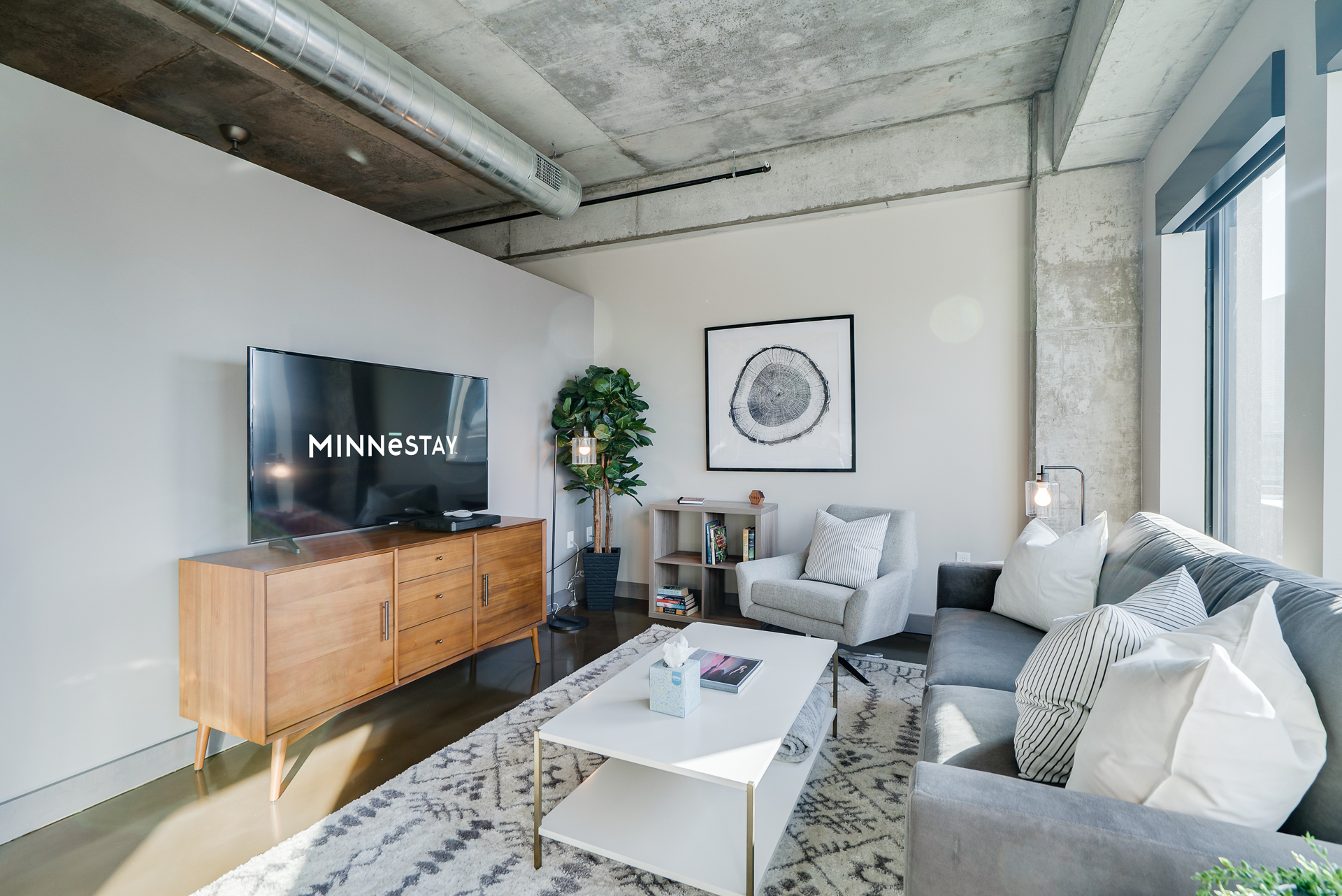 Stylish modern living room with concrete ceiling, wooden media console, and cozy seating.