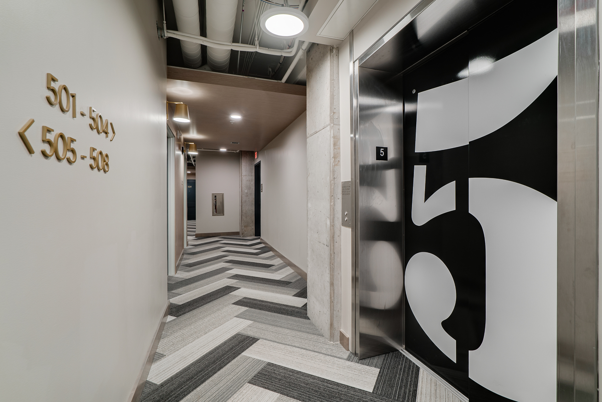 Contemporary hallway with stylish elevator doors and room signage.