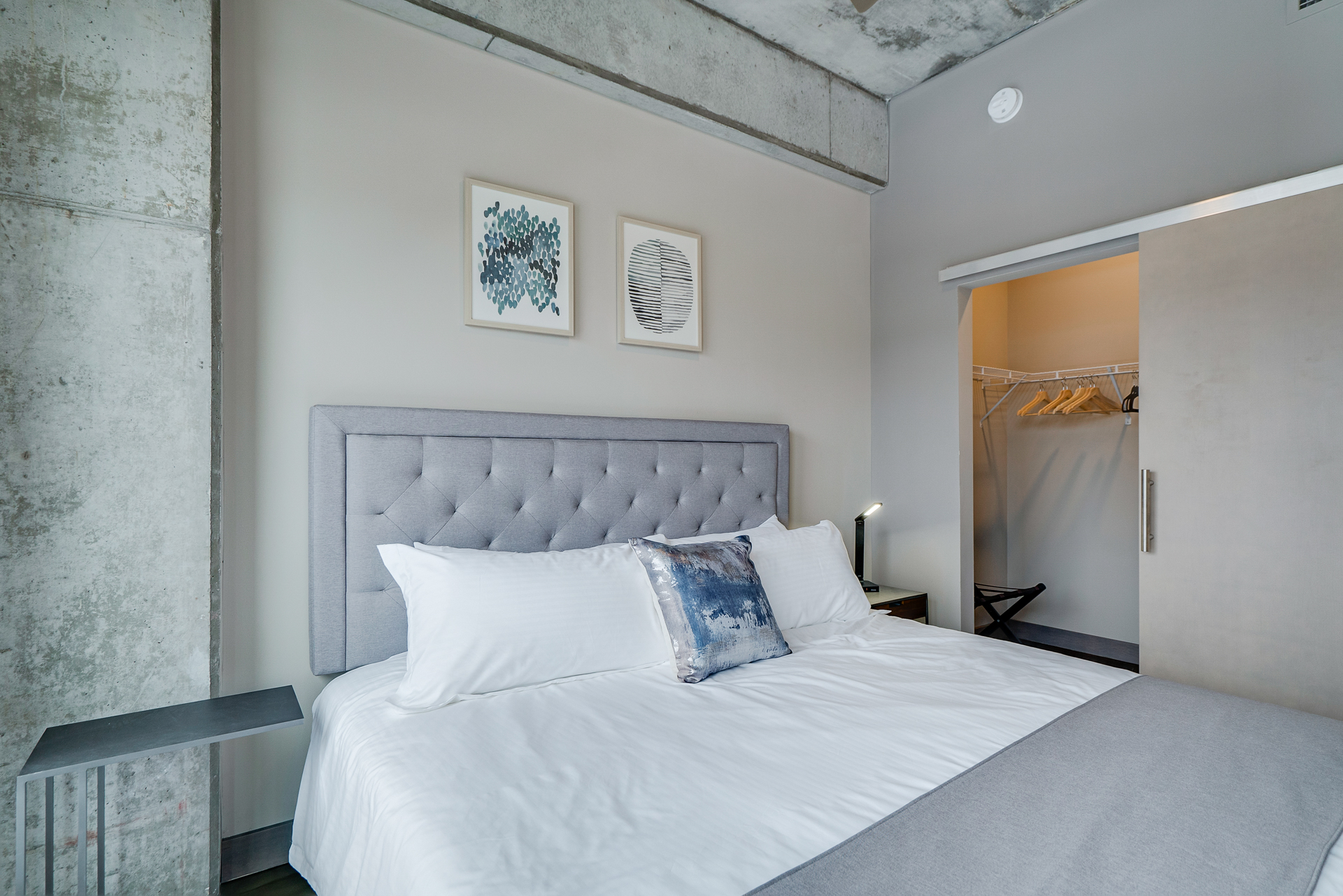 A stylish modern bedroom with a minimalist design featuring a tufted gray headboard and blue decorative pillow.