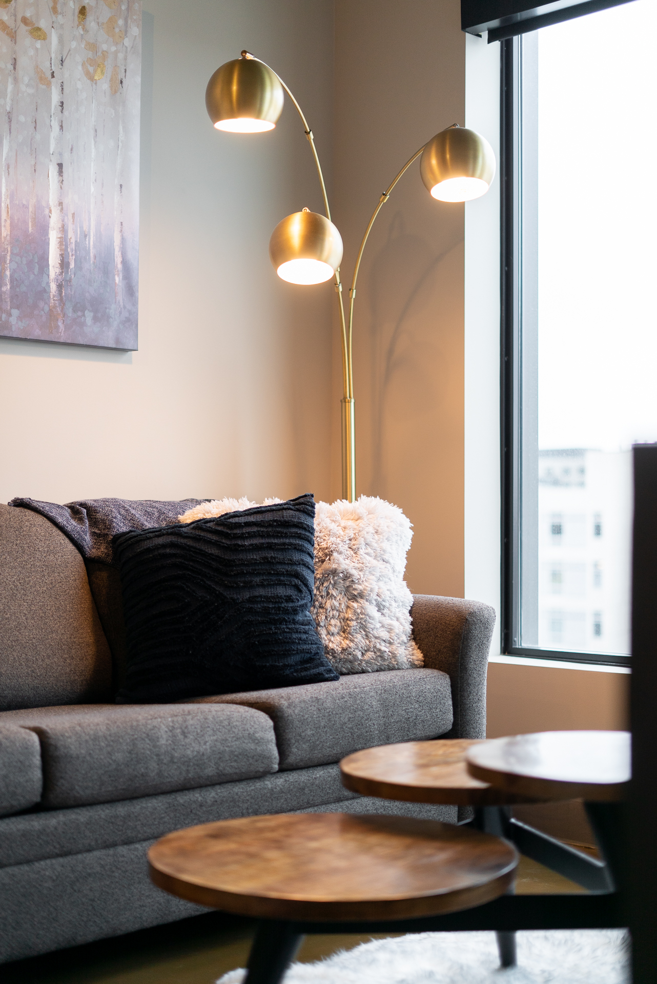 A stylish living room corner with a grey sofa, golden floor lamp, and warm decorative elements.