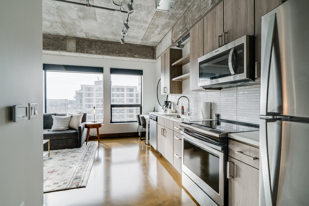 Stylish kitchen and living area with modern appliances and large windows in an apartment.
