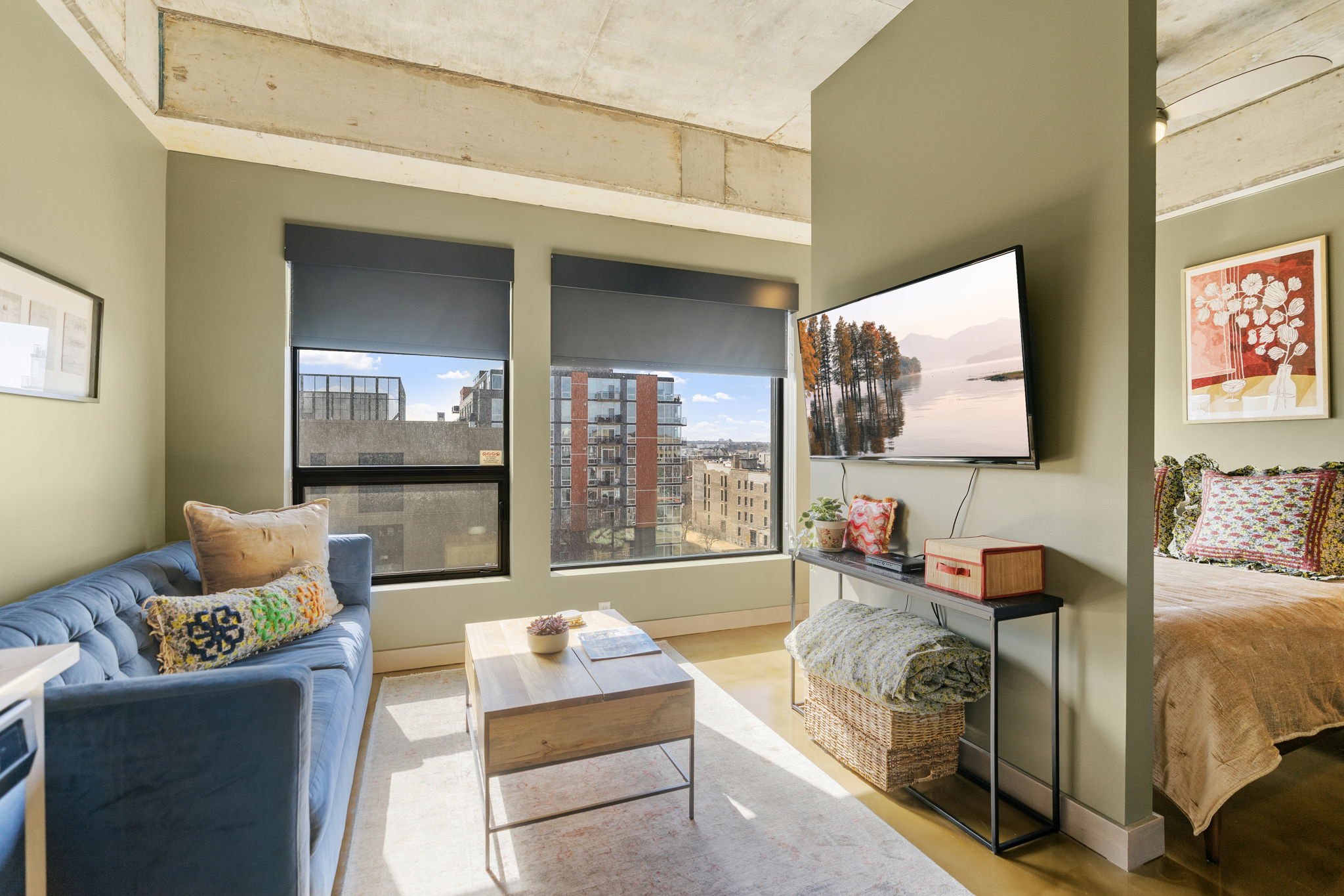 A modern and cozy living space with a blue couch, wall-mounted TV, and a bed nearby.