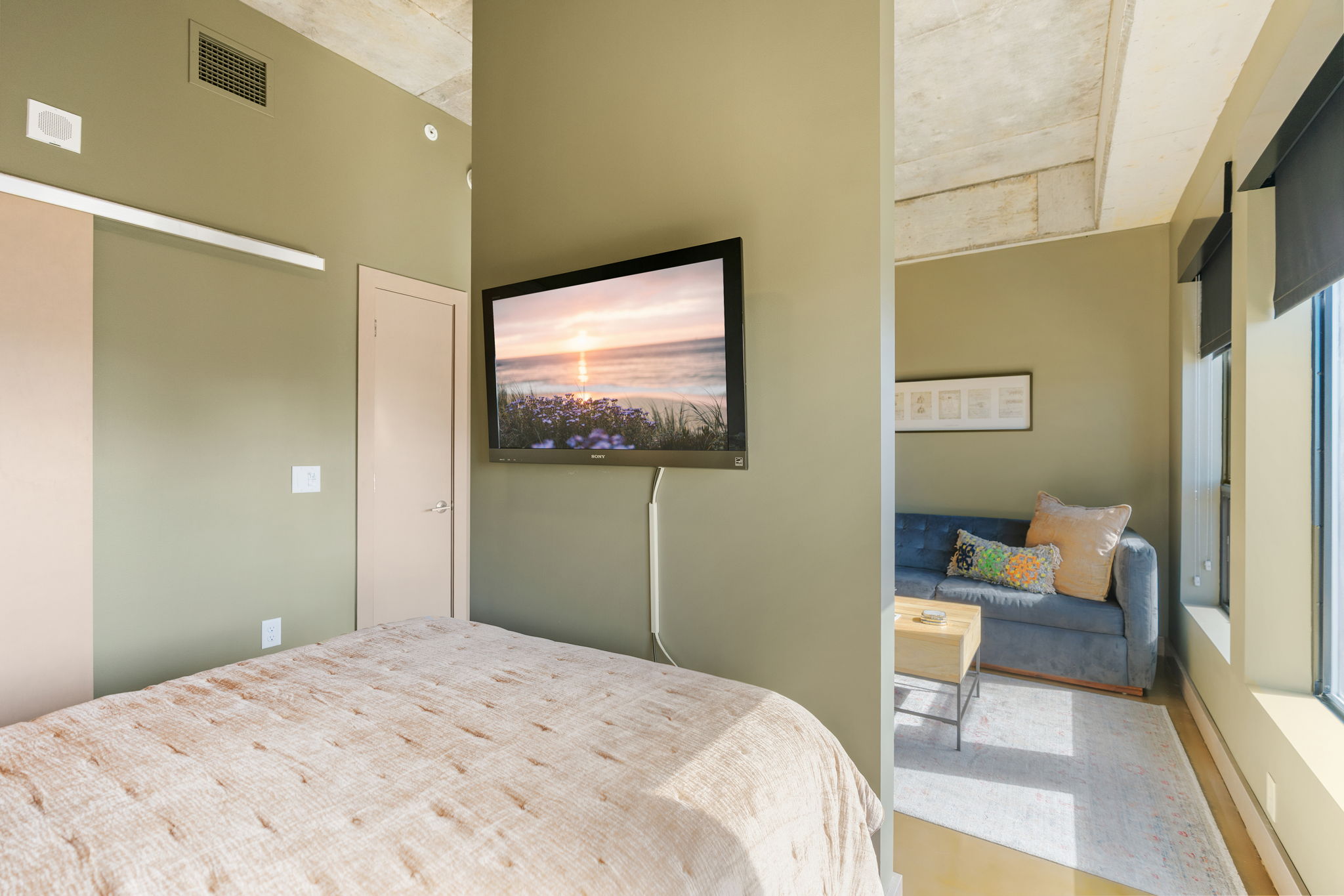 Modern bedroom with a cozy living area, featuring a serene seaside sunset on the TV.