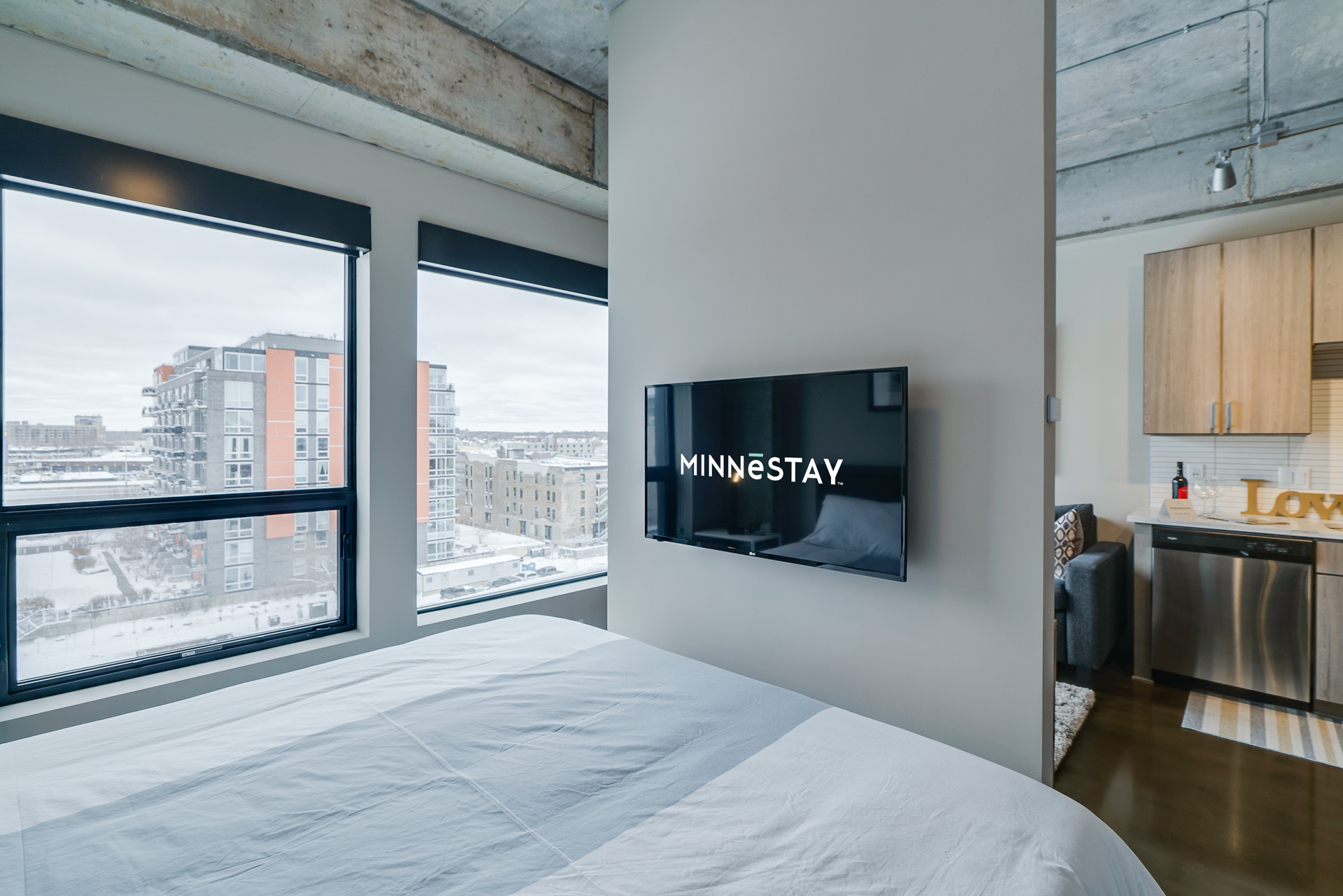 Modern bedroom with a snowy city view and a TV displaying 'MINNESTAY.'