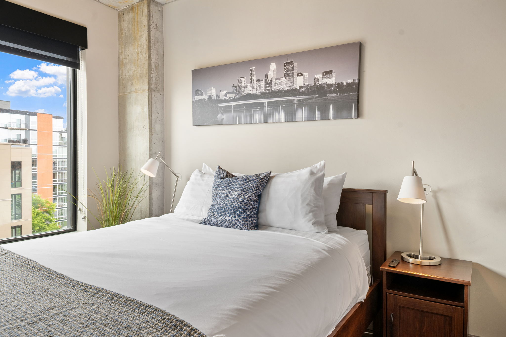 A serene bedroom featuring a cozy bed and a city skyline artwork.