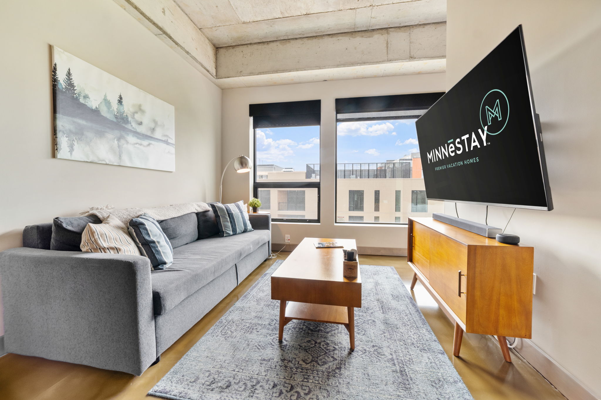A stylish and modern living room with a gray sofa, wooden coffee table, and large windows.