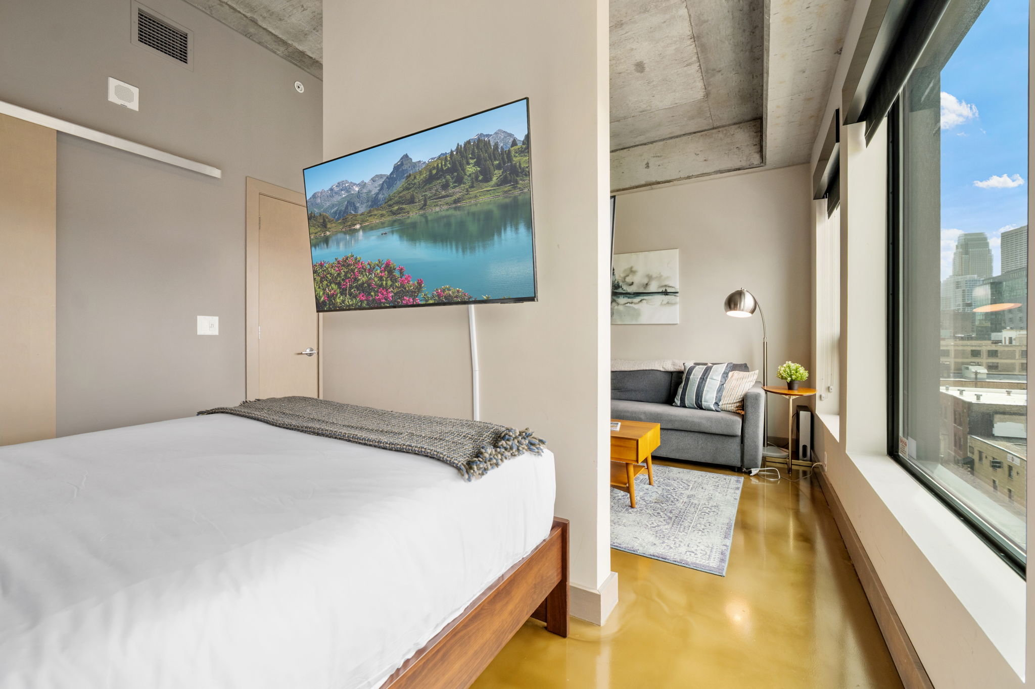 A modern studio apartment featuring a bed, living area, and scenic TV view.