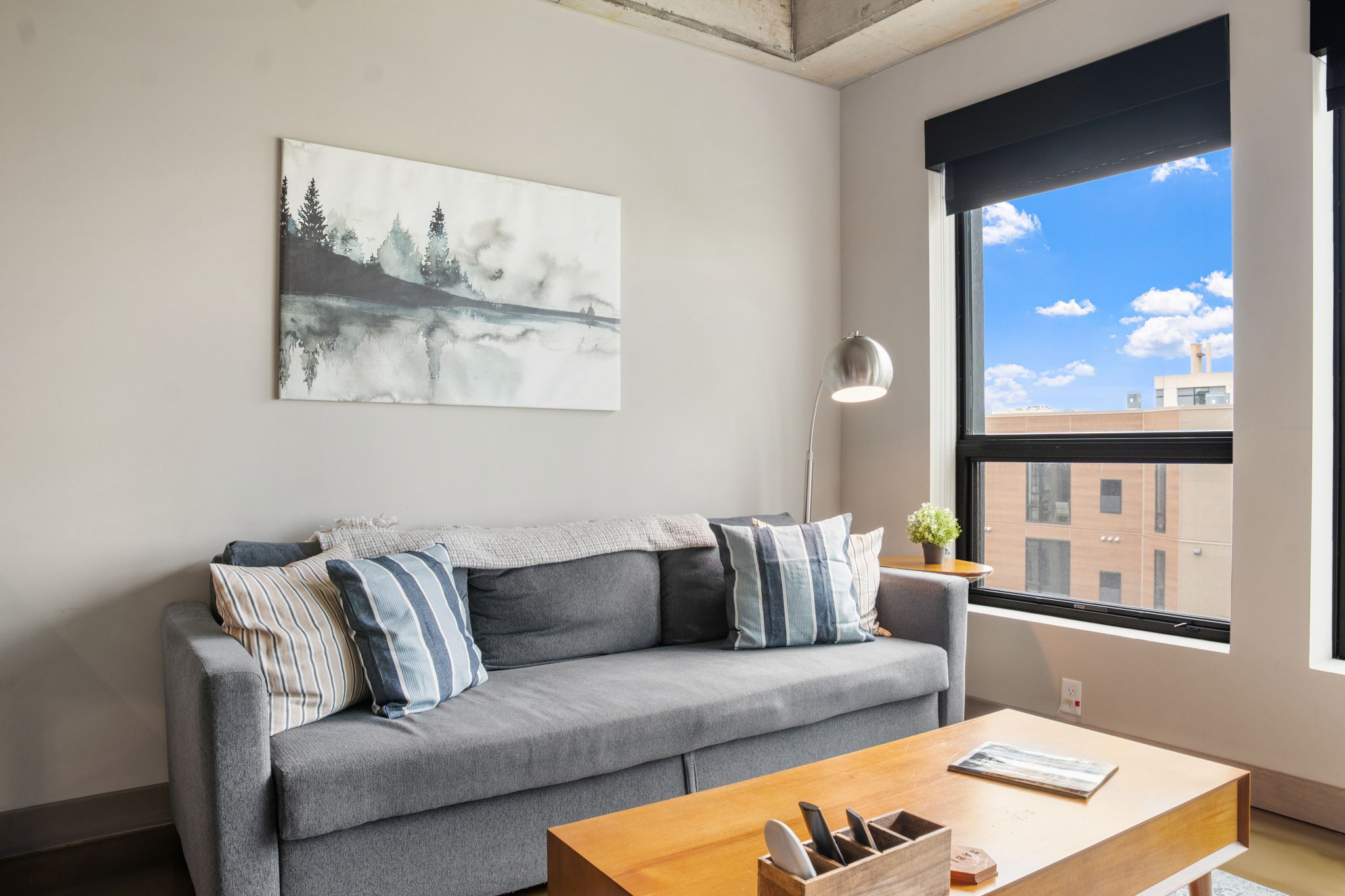 A cozy modern living room with a gray sofa and a serene landscape artwork.