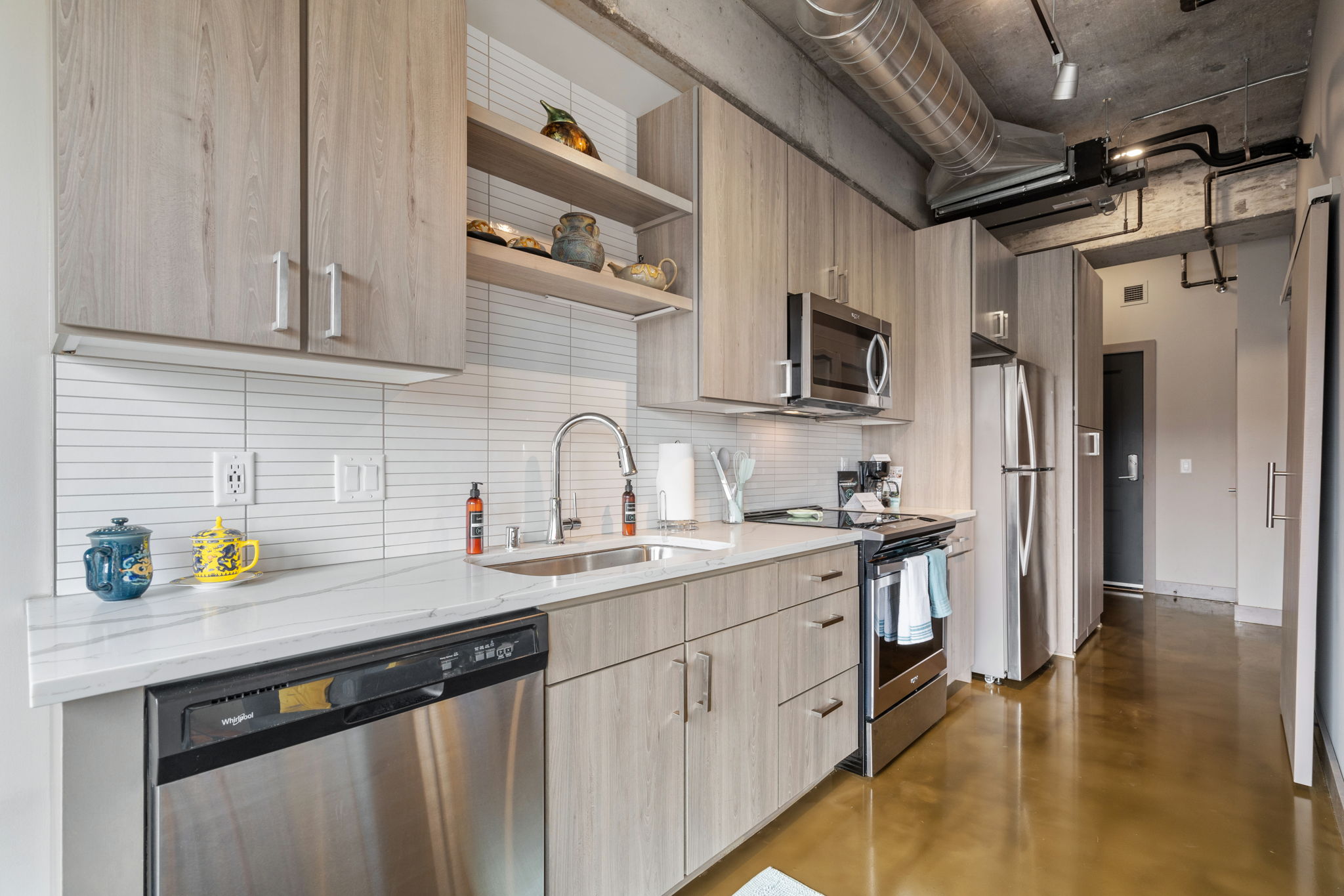 Modern kitchen with light wood cabinetry and stainless steel appliances.