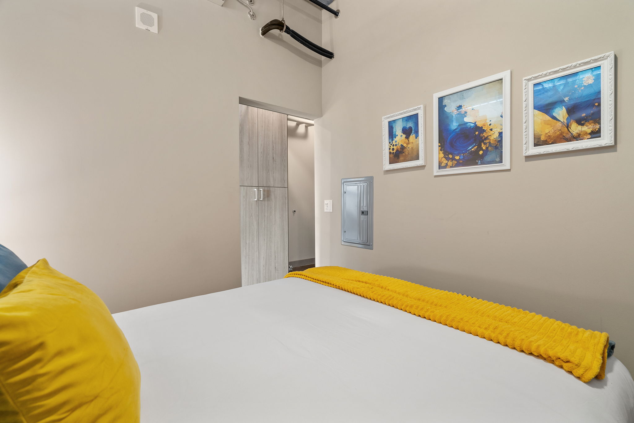 A cozy modern bedroom with a white bed, vibrant yellow blanket, and framed artworks on the wall.