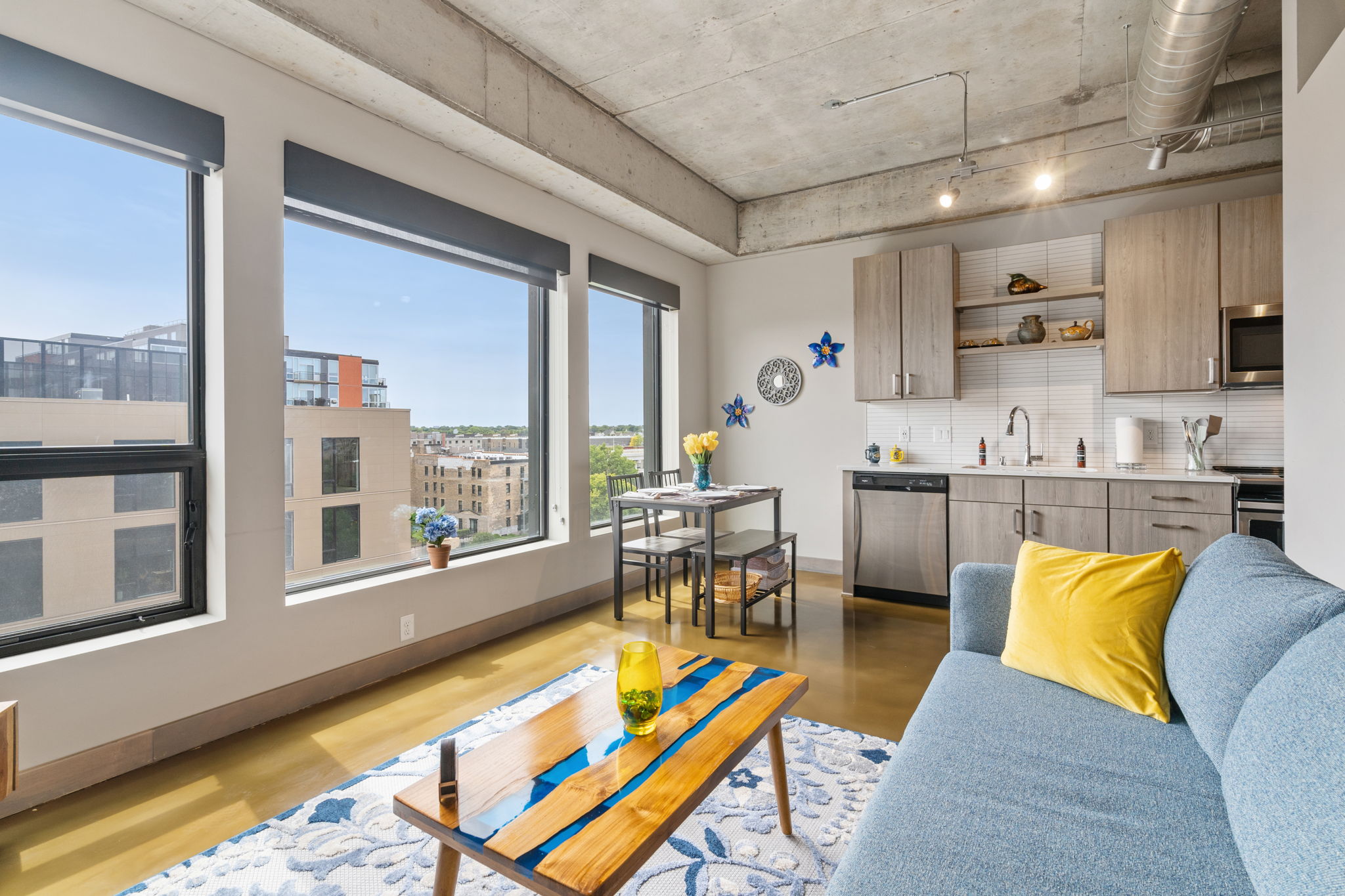 Stylish apartment featuring large windows, a blue couch, and a wooden dining table.